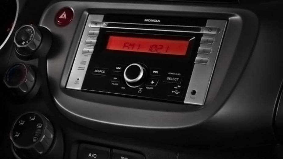 Rádio da versão LX está integrado ao console e vem com entrada USB | <a href="https://beta-develop.quatrorodas.abril.com.br/carros/lancamentos/honda-fit-2013-680204.shtml" rel="migration">Leia mais</a>