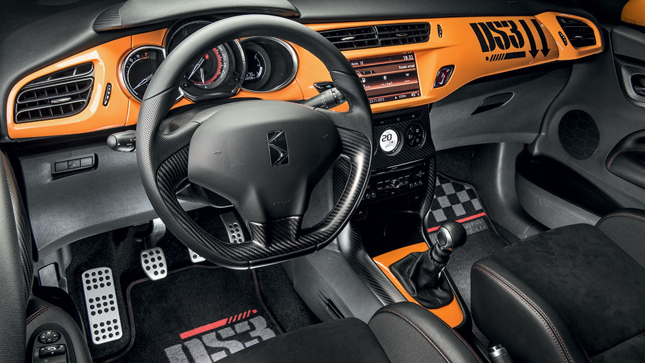 Tapetes, painel e volante seguem a decoração da carroceria, com fibra de carbono, pintura laranja e grafismo militar | <a href="https://beta-develop.quatrorodas.abril.com.br/carros/testes/citroen-ds3-racing-728659.shtml" rel="migration">Leia mais</a>