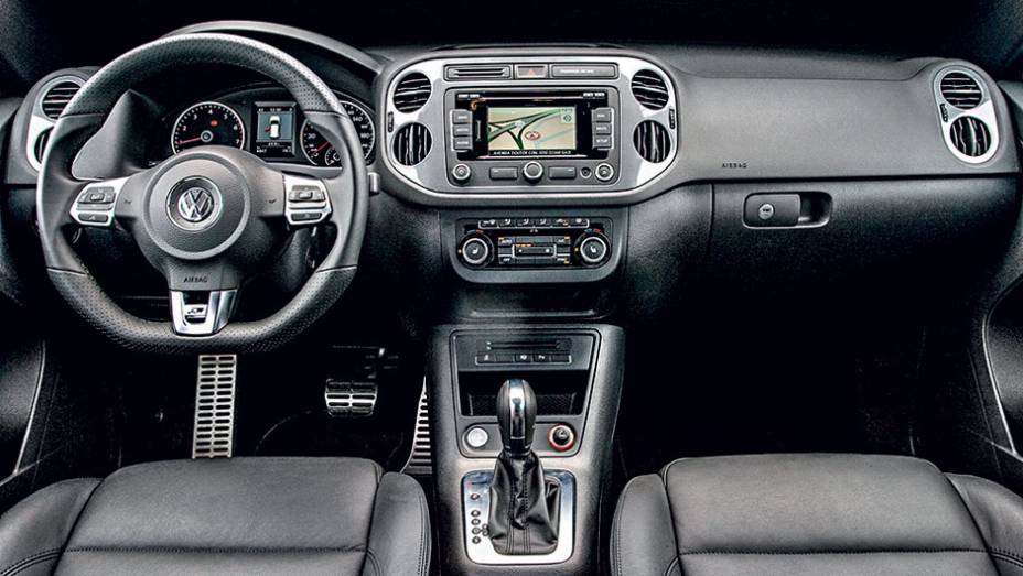 Interior possui volante de três raios com base achatada | <a href="https://beta-develop.quatrorodas.abril.com.br/carros/lancamentos/vw-tiguan-r-line-726908.shtml" rel="migration">Leia mais</a>