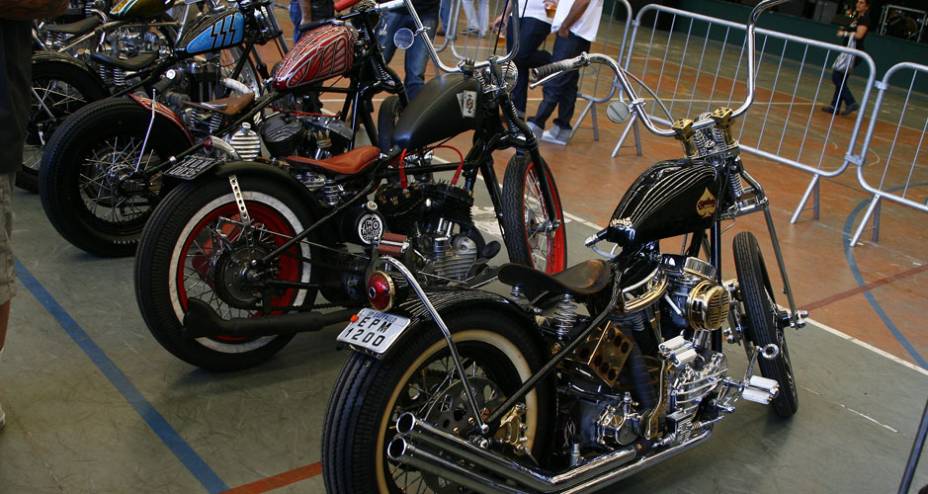 Choppers com frente springer e guidão elevado, quadro rabo duro, pneus faixa branca e motores H-D de diferentes gerações | <a href="https://beta-develop.quatrorodas.abril.com.br/moto/noticias/two-wheels-brazil-reune-fabricantes-nacionais-americanos-motos-vintage-644346." rel="migration"></a>