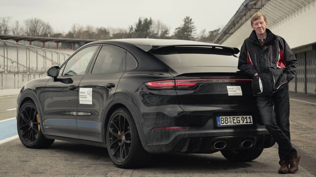 Walter Röhrl ao lado direito do Porsche Cayenne Coupé Turbo preto visto de trás