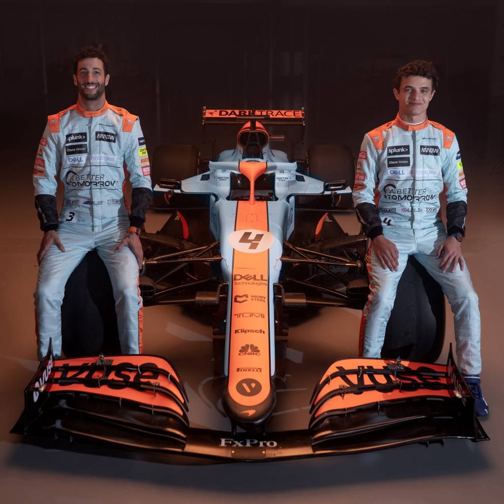 Daniel Ricciardo e Lando Norris com pintura gulf Daniel Ricciardo e Lando Norris sentados no carro de Fórmula 1 da McLaren visto de frente