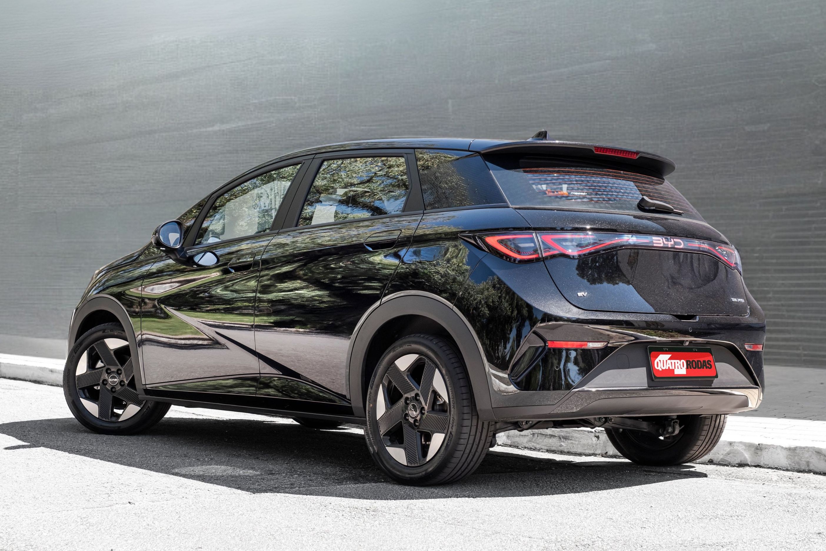 Carro preto brilhante, modelo SUV compacto, visto de tr&aacute;s e lateral, estacionado em asfalto cinza com meio-fio branco, contra parede cinza. As lanternas traseiras s&atilde;o vermelhas e o para-choque tem detalhes cromados. As rodas s&atilde;o pretas com design de cinco raios