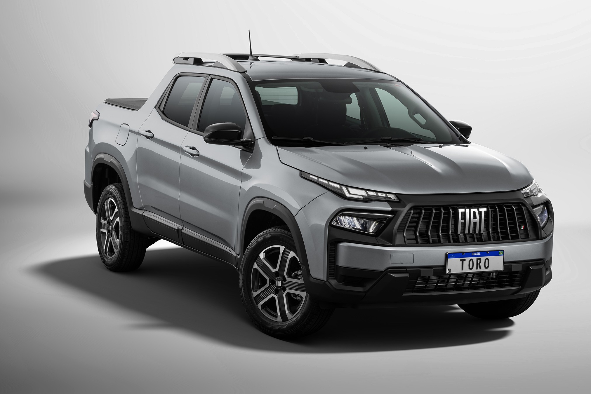 Picape Fiat Toro cinza-prata, vista de frente e lateralmente, com rack de teto, capota mar&iacute;tima e placa 