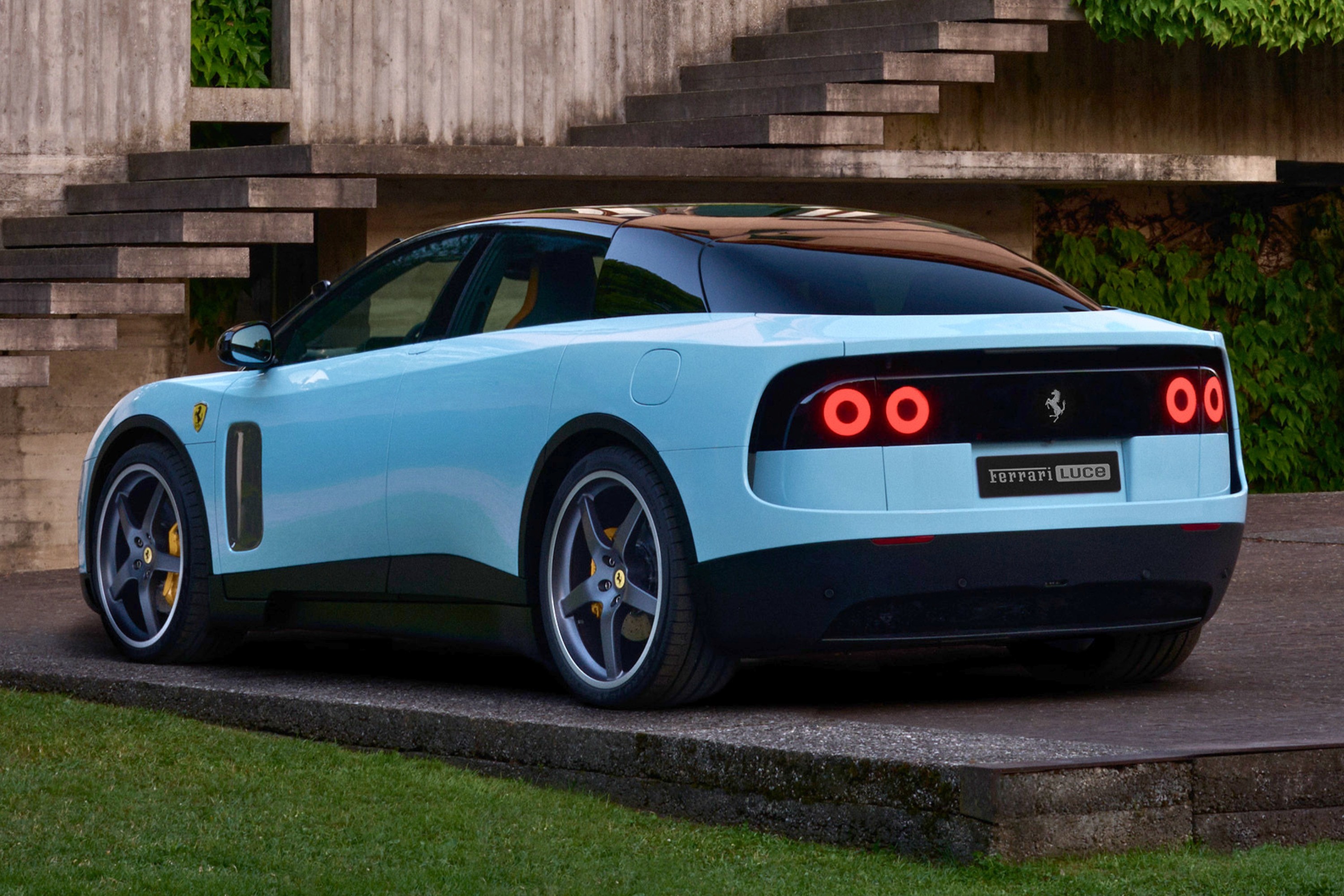 Carro esportivo Ferrari Luce azul-claro com teto preto, visto de traseira lateral, estacionado em uma rampa de concreto com grama ao lado. Ao fundo, uma escadaria de concreto e folhagem verde