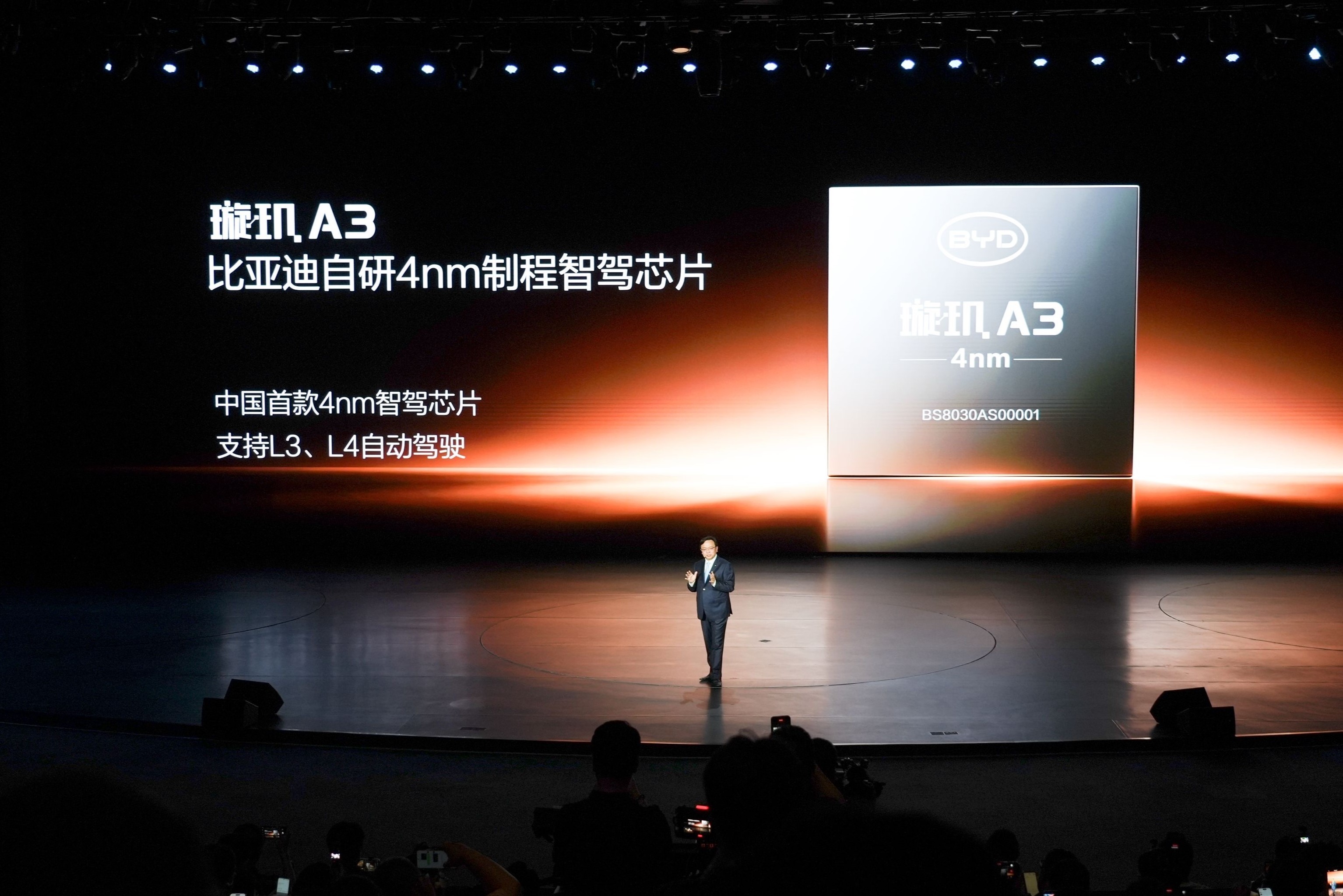 Homem de terno escuro em palco escuro com tela gigante exibindo o chip BYD Xuanji A3 de 4nm para dire&ccedil;&atilde;o aut&ocirc;noma L3 e L4
