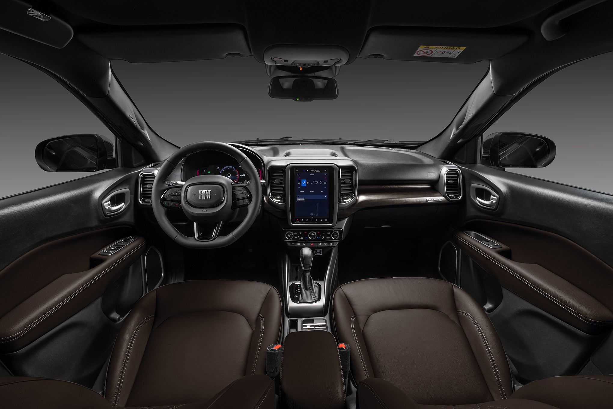 Interior de um carro moderno com bancos de couro marrom, painel escuro, volante multifuncional com logo Fiat e tela multim&iacute;dia vertical no centro