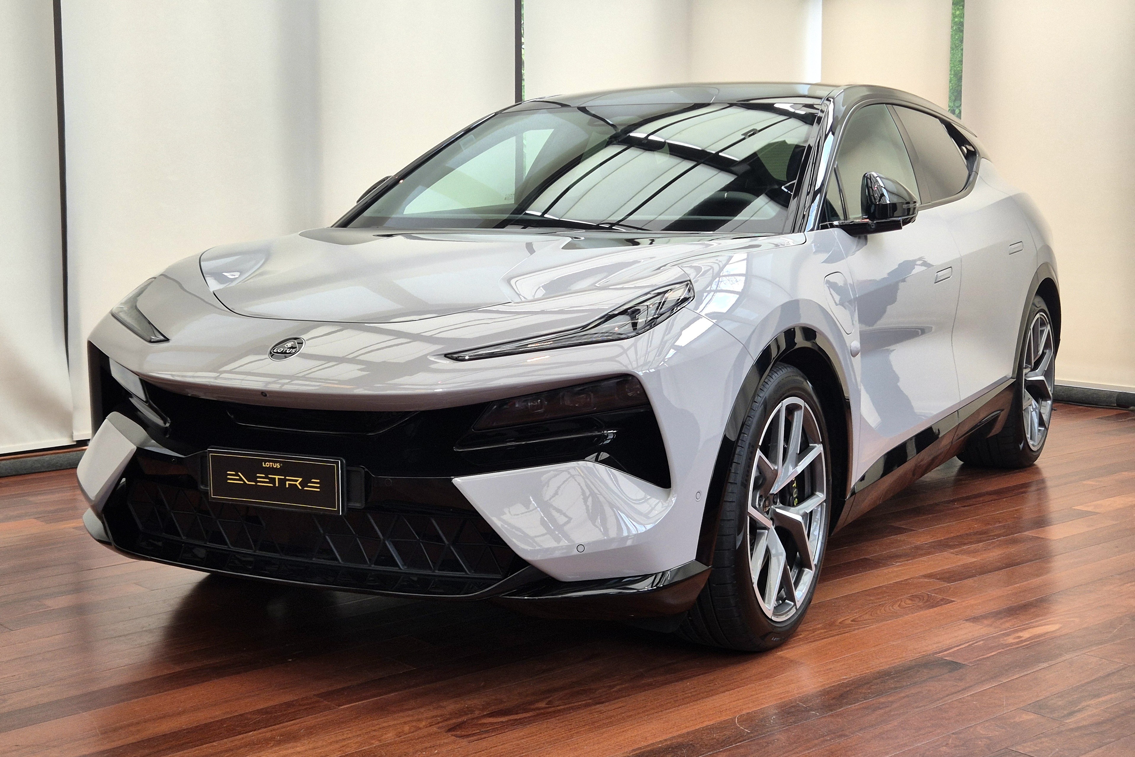 SUV el&eacute;trico Lotus Eletre cinza claro, com teto e detalhes pretos, estacionado em piso de madeira marrom brilhante