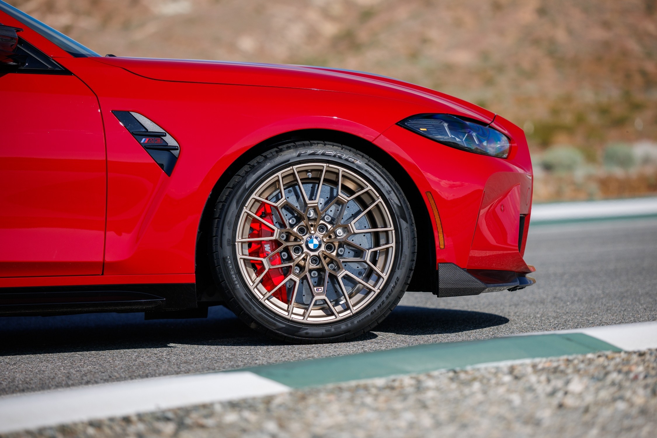 Lateral de um carro esportivo vermelho brilhante, com roda de liga leve dourada e pin&ccedil;a de freio vermelha, parado em uma pista de asfalto com faixa branca e verde