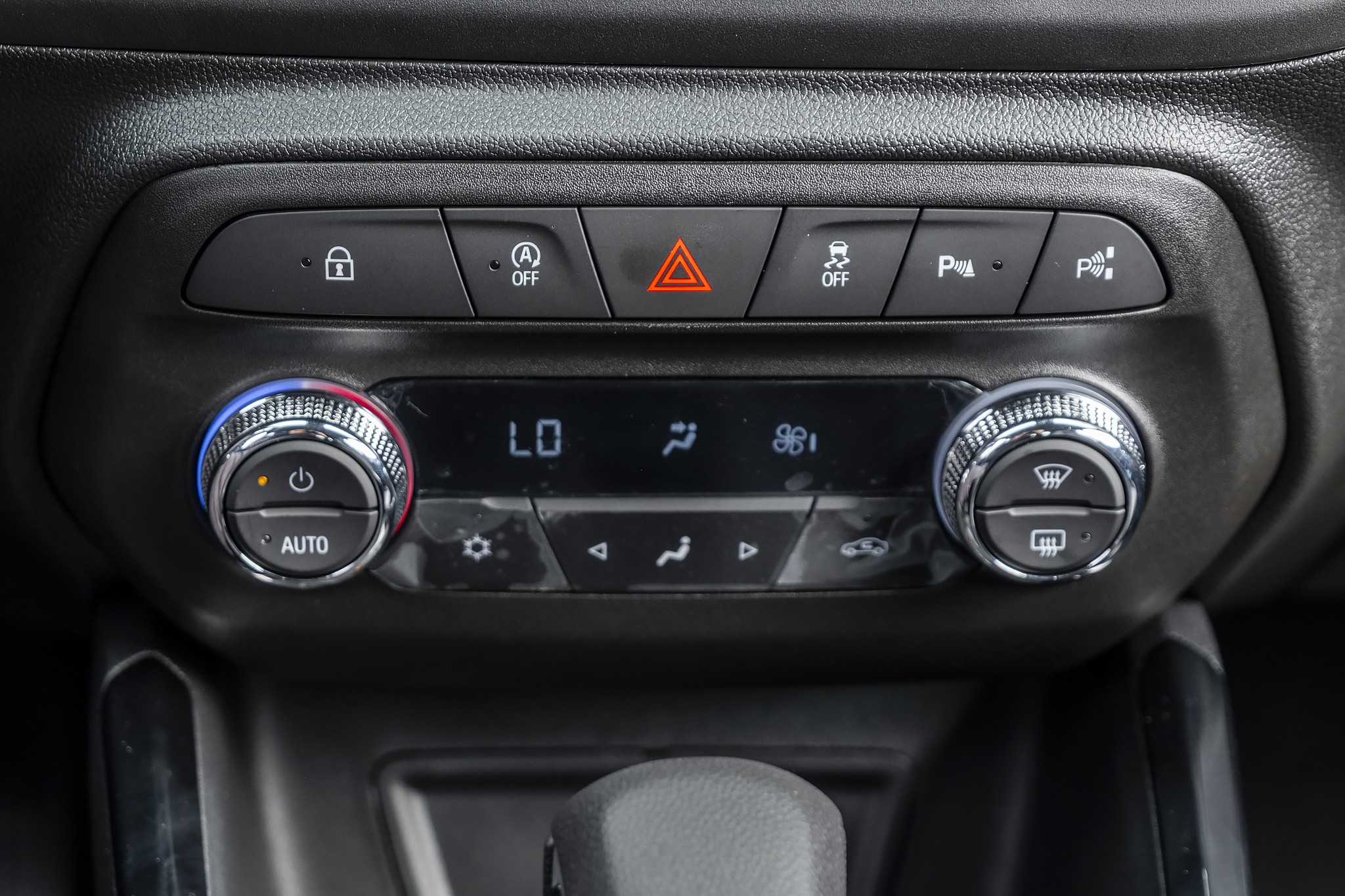 Painel de controle do ar-condicionado e fun&ccedil;&otilde;es do carro, com bot&otilde;es para travar portas, ligar/desligar motor, pisca-alerta, controle de estabilidade e sensores de estacionamento. O display mostra 