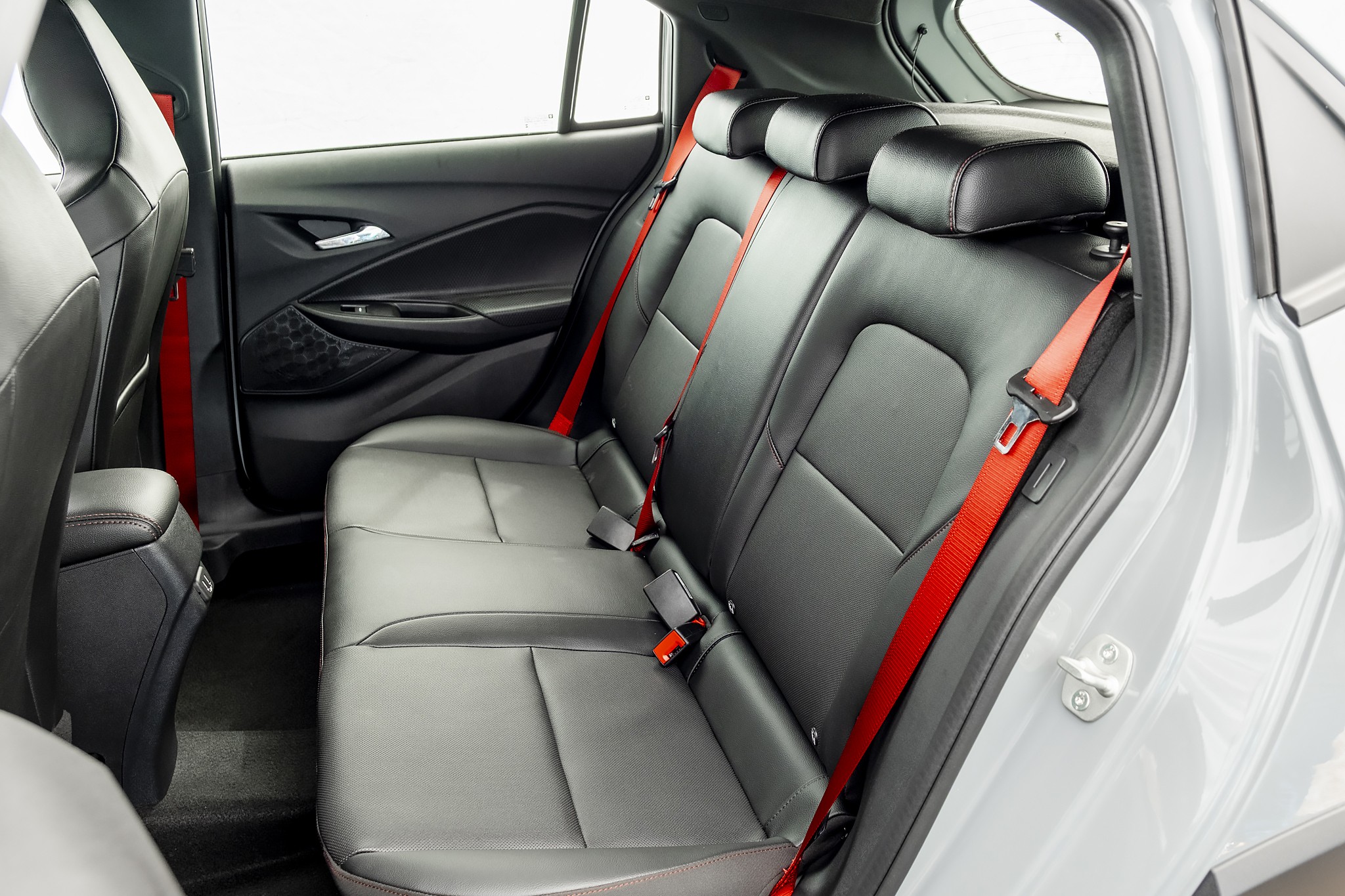 Interior de um carro com bancos traseiros de couro preto e cintos de seguran&ccedil;a vermelhos, destacando o contraste de cores e o design moderno