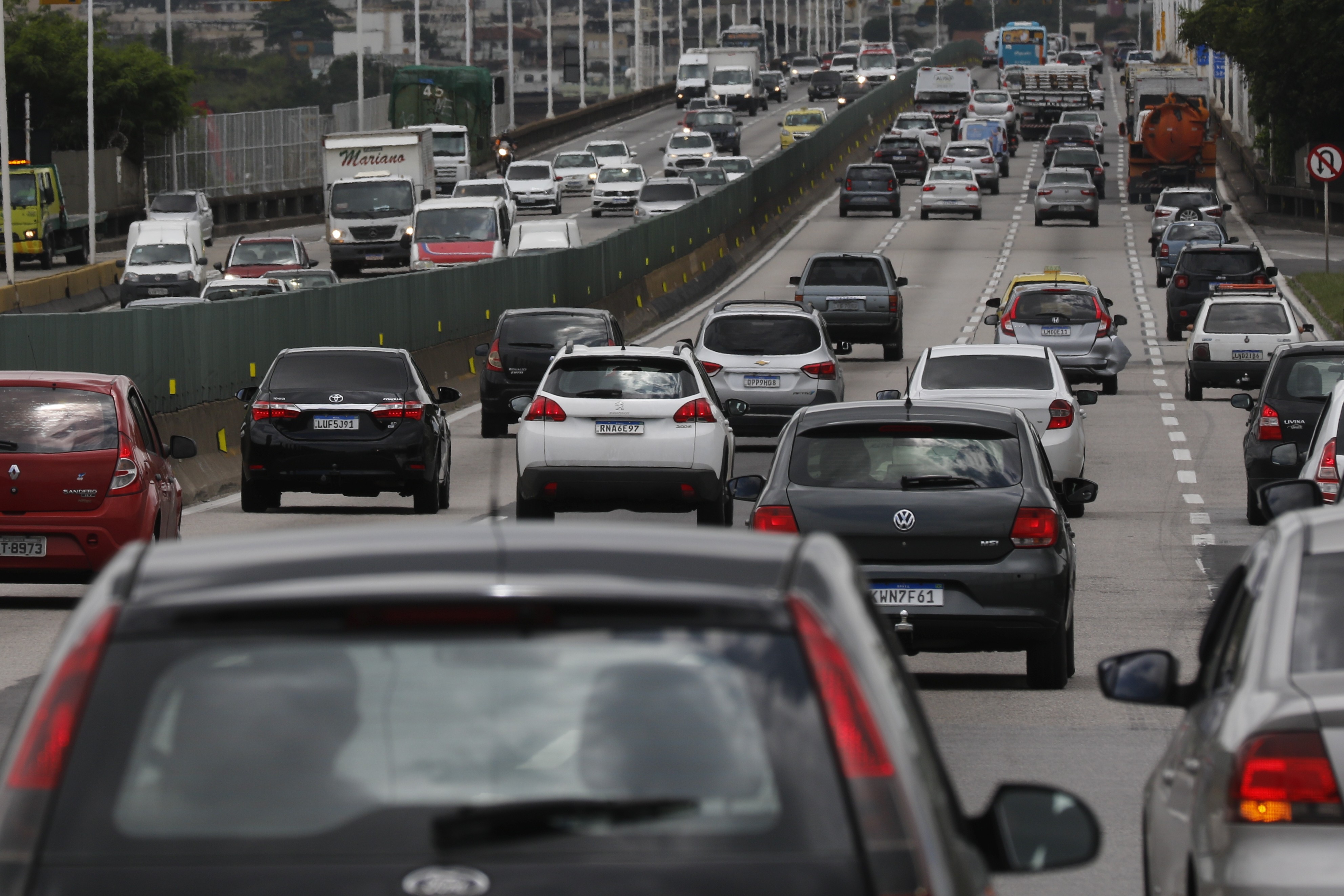 Tr&aacute;fego intenso de ve&iacute;culos em uma rodovia com v&aacute;rias pistas, carros e caminh&otilde;es em movimento lento, sob um c&eacute;u nublado