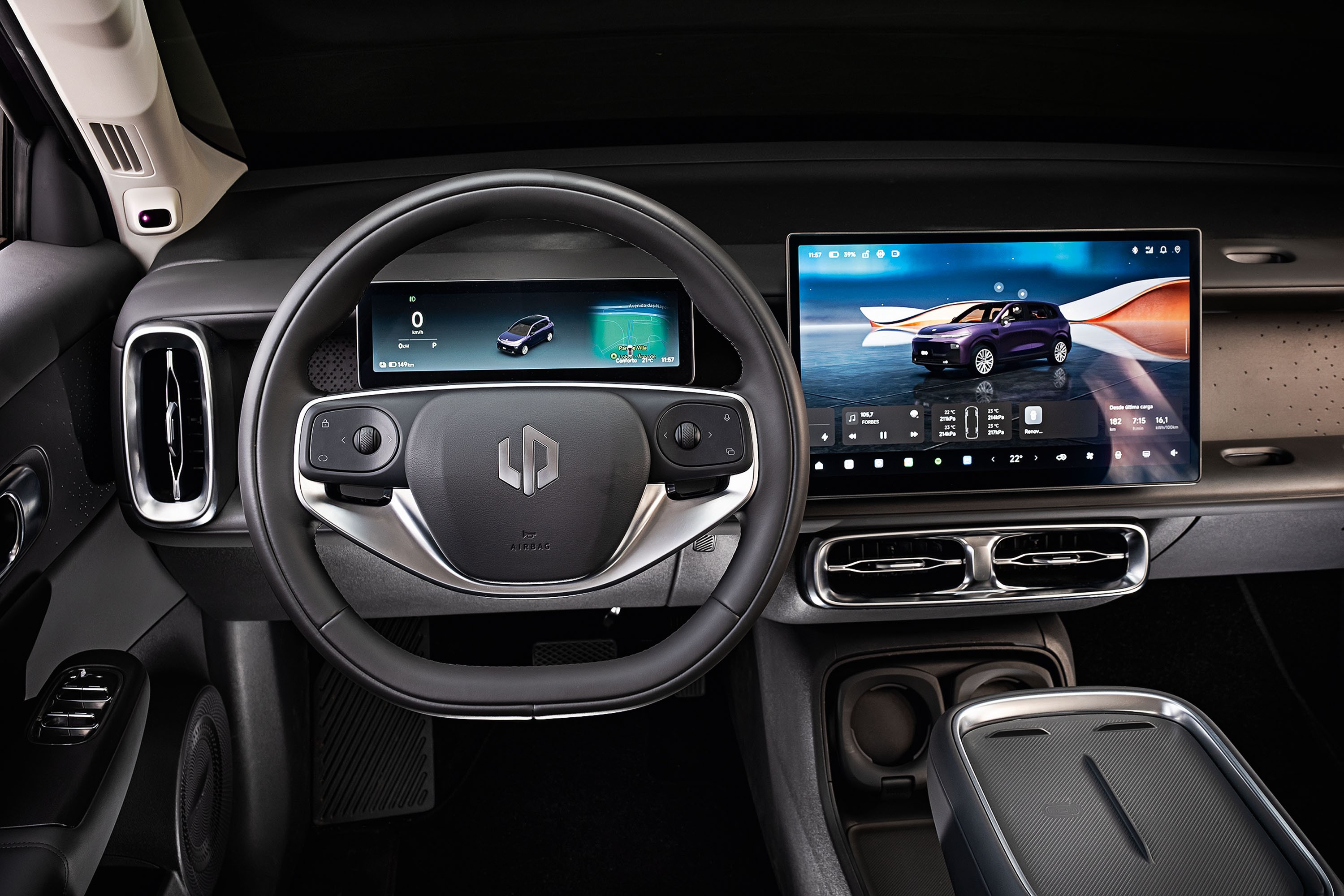 Interior de um carro moderno com volante preto e cinza, painel digital exibindo um carro roxo e tela multim&iacute;dia grande com o mesmo ve&iacute;culo. Detalhes de sa&iacute;das de ar cromadas e console central com porta-copos.