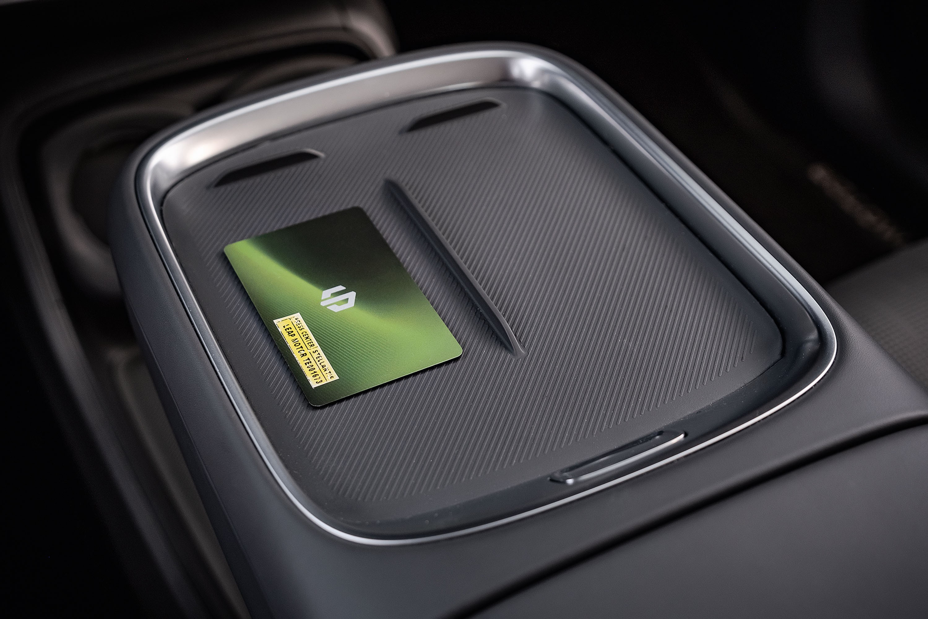 Cart&atilde;o verde met&aacute;lico com logo branco e adesivo amarelo sobre console central cinza escuro texturizado de carro, com detalhes prateados e uma caneta preta fina ao lado