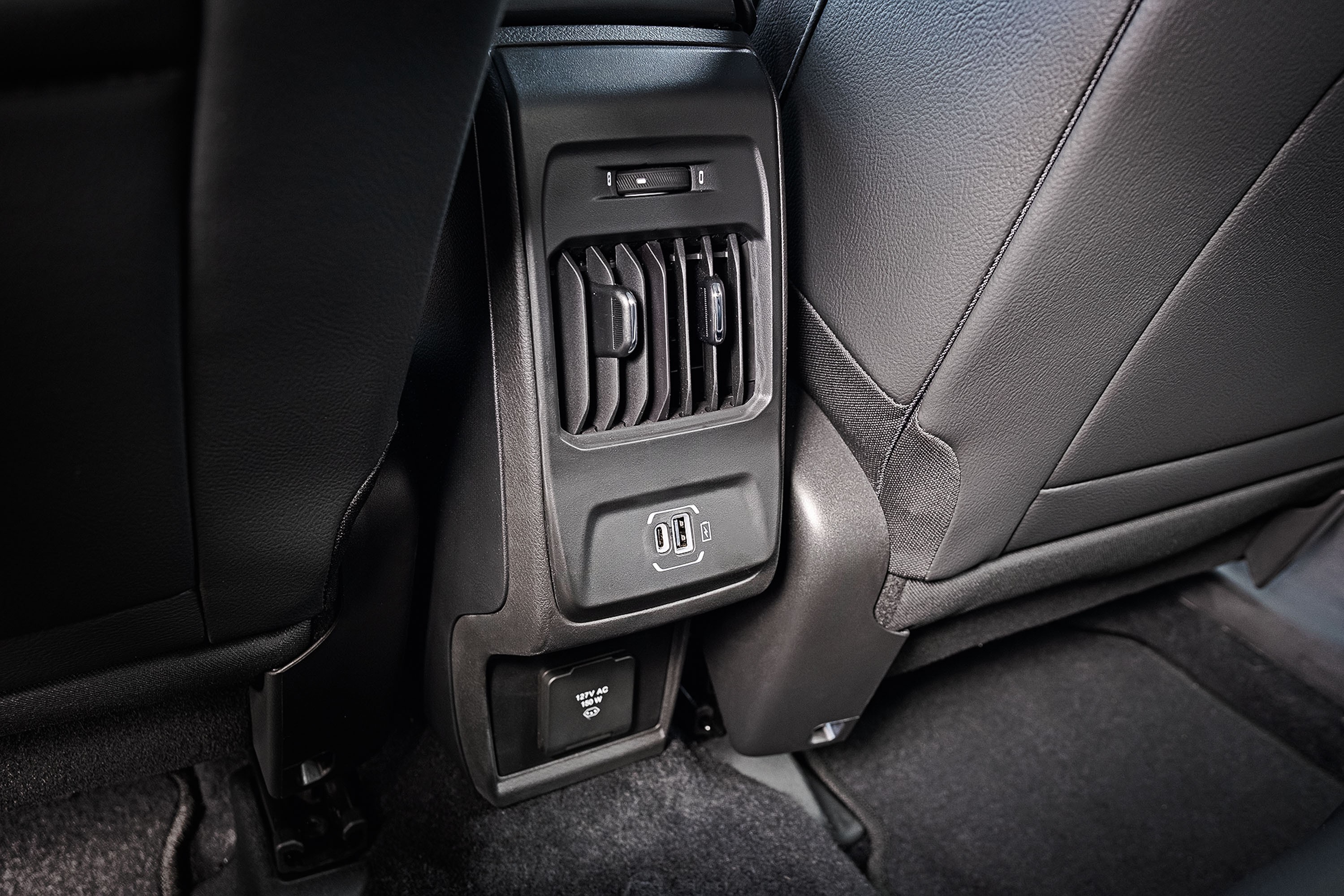 Painel traseiro de um carro com sa&iacute;das de ar, duas portas USB e uma tomada de 12V, entre dois bancos de couro preto