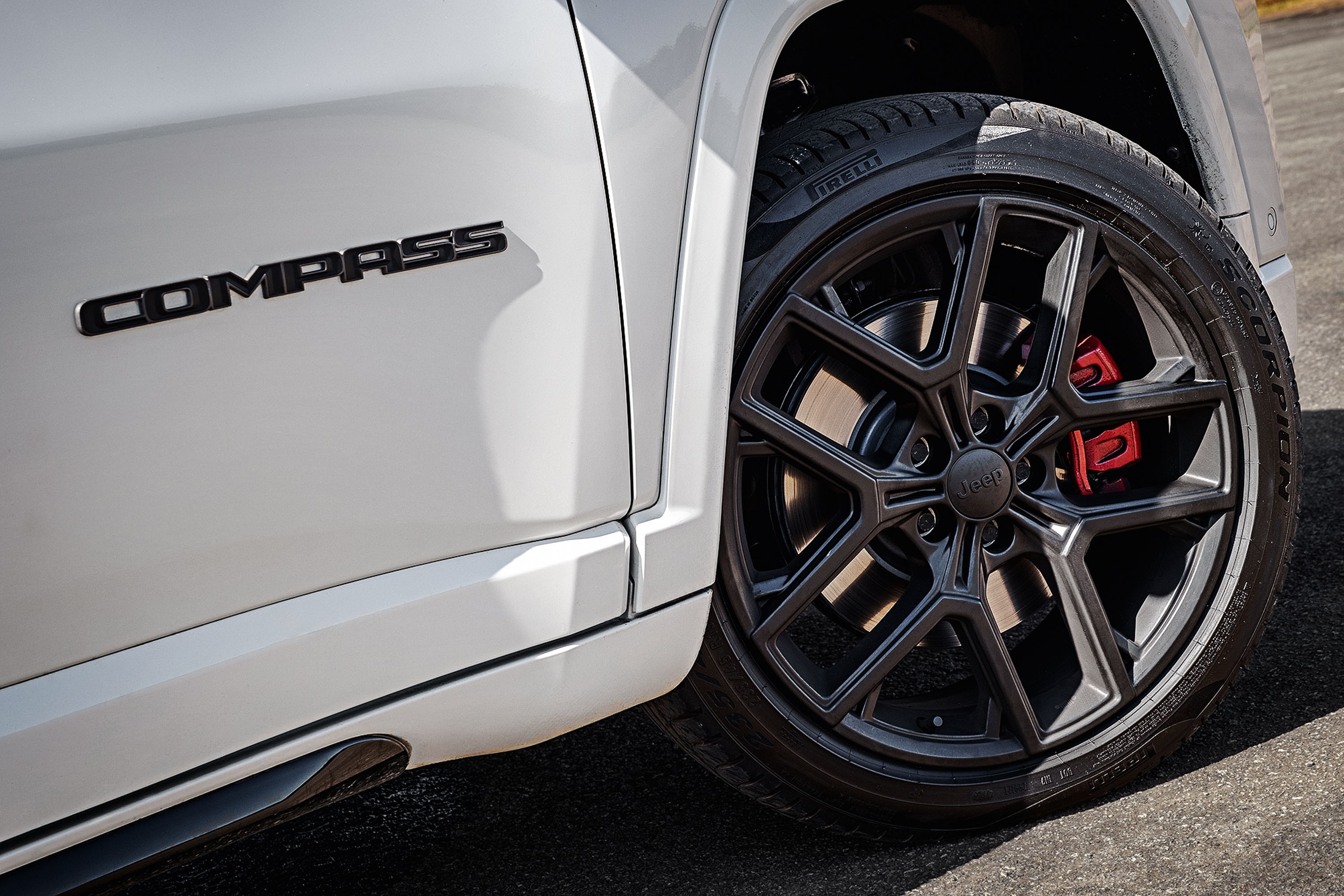 Lateral de um carro branco com o emblema COMPASS em preto, pr&oacute;ximo a uma roda preta com detalhes em vermelho nos freios