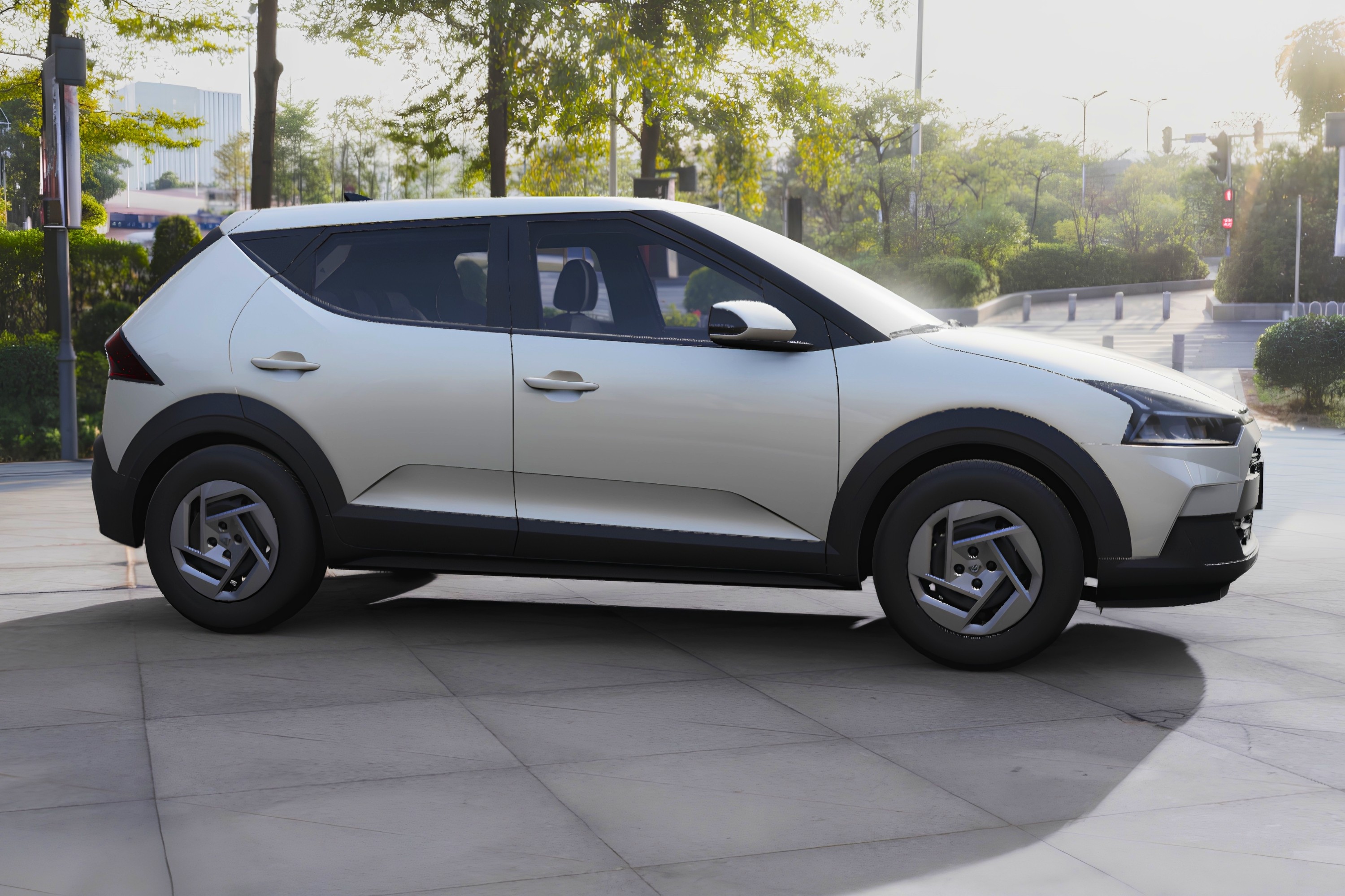 Carro SUV compacto prateado, com detalhes em preto nas caixas de roda e parte inferior, estacionado em cal&ccedil;ada de concreto. Ao fundo, &aacute;rvores e uma rua com sem&aacute;foro vermelho, sob luz solar