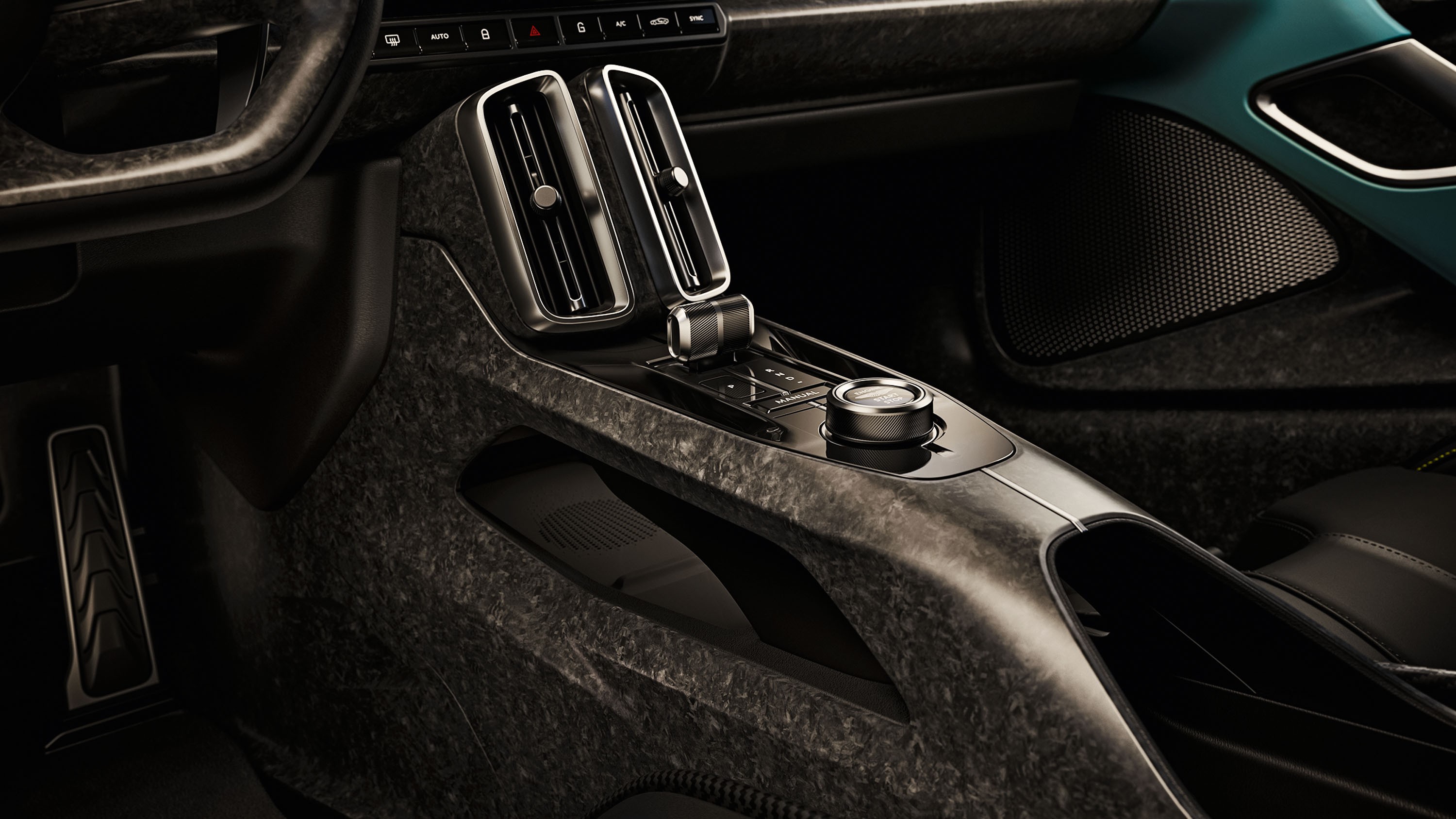 Interior de carro moderno com console central em tom escuro texturizado, dois difusores de ar verticais, alavanca de c&acirc;mbio e um bot&atilde;o girat&oacute;rio prateado. O volante e o pedal esquerdo s&atilde;o vis&iacute;veis, com detalhes em azul-petr&oacute;leo na porta direita