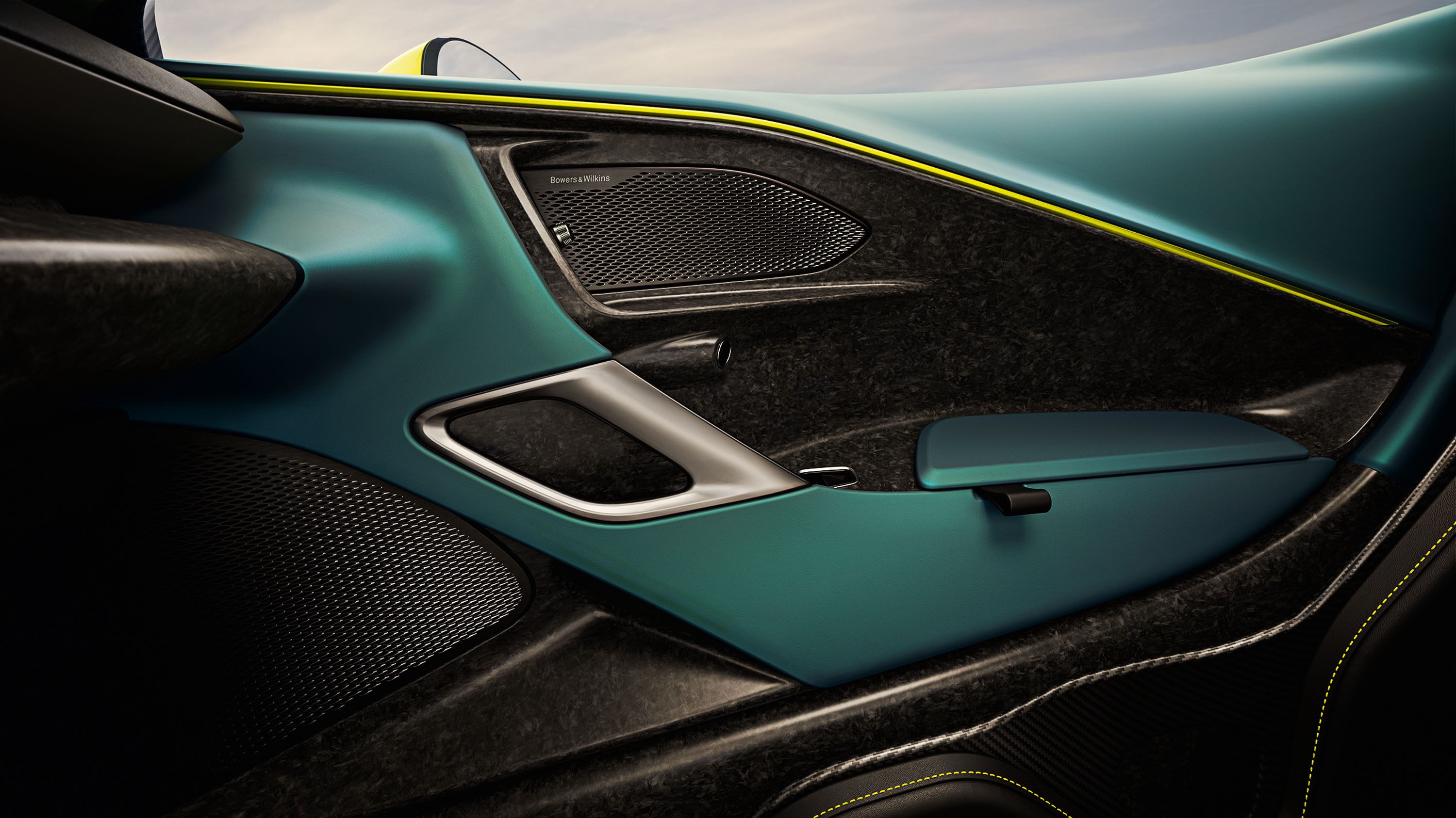 Interior de carro esportivo com porta em tons de azul-petr&oacute;leo e preto, detalhes em fibra de carbono e costura amarela. H&aacute; uma al&ccedil;a de porta prateada e dois alto-falantes com grade met&aacute;lica. O design &eacute; moderno e luxuoso