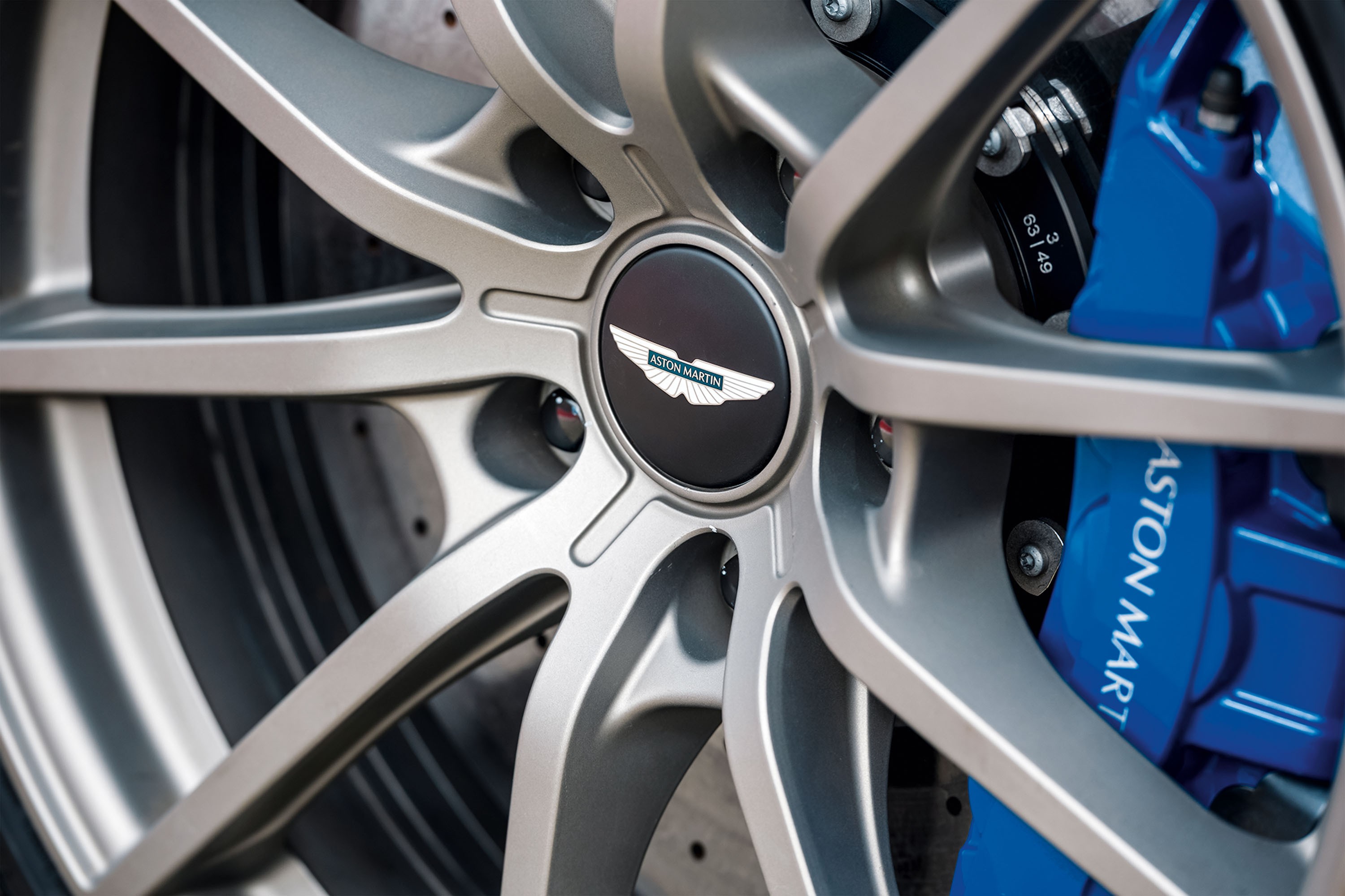 Roda de carro esportivo Aston Martin com aro cinza-chumbo de m&uacute;ltiplos raios, pin&ccedil;a de freio azul brilhante e o logotipo da marca no centro