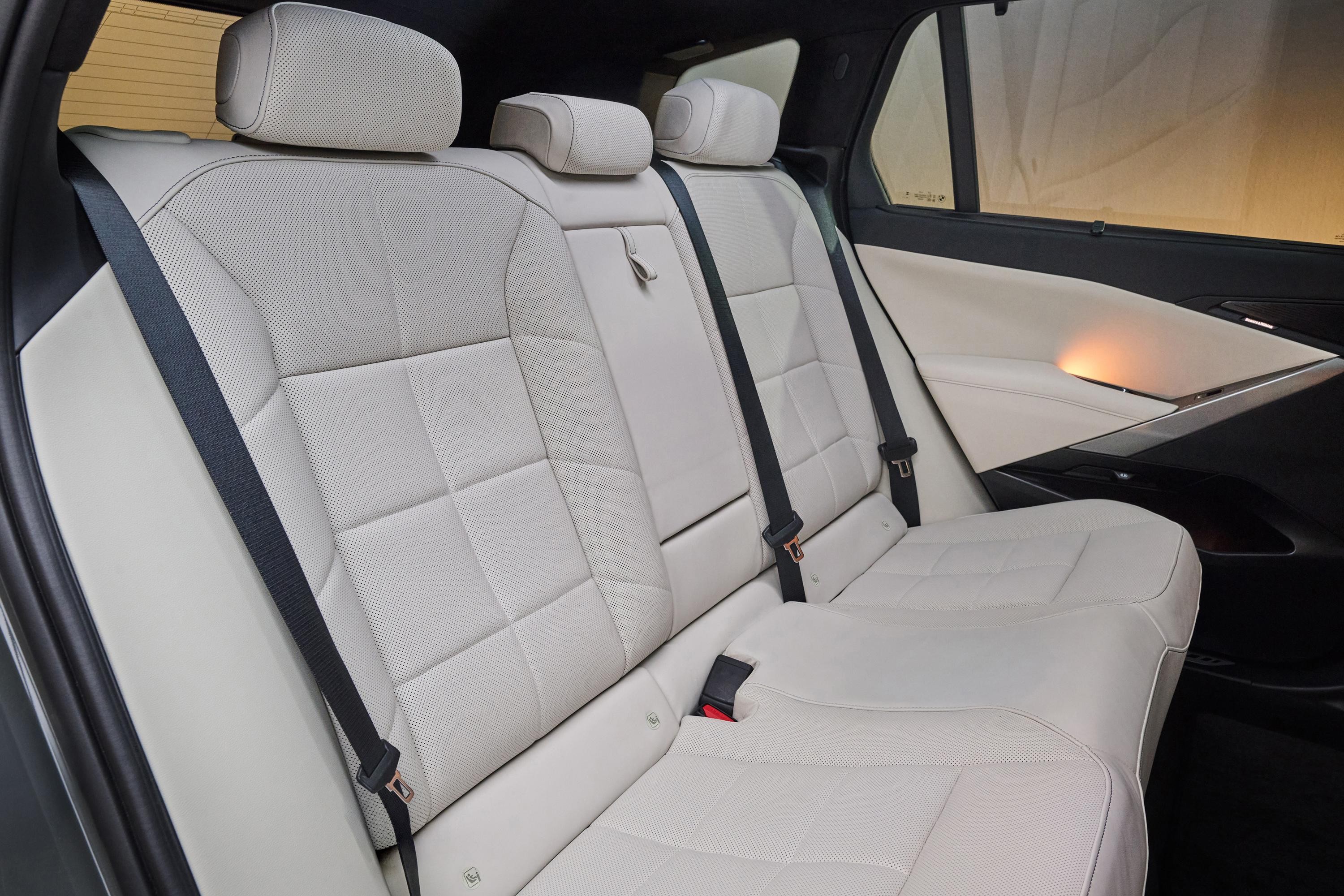 Interior de carro com bancos traseiros de couro branco perfurado, costuras em padr&atilde;o geom&eacute;trico e cintos de seguran&ccedil;a pretos. A porta lateral tem acabamento em branco e preto com ilumina&ccedil;&atilde;o ambiente laranja suave
