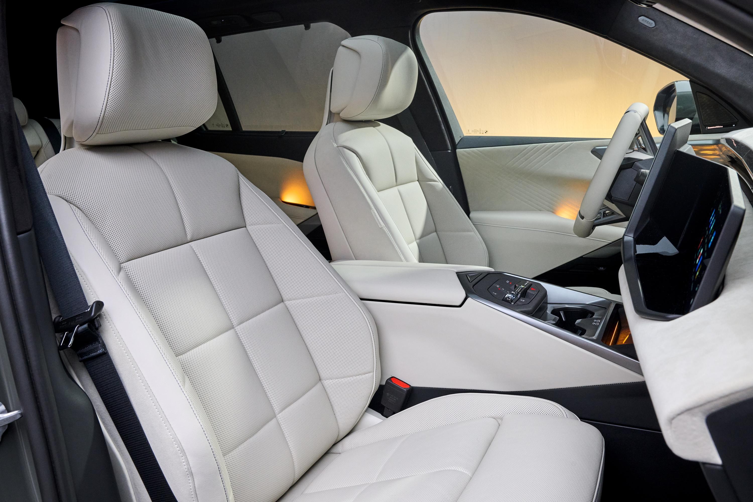 Interior de carro moderno com bancos de couro branco acolchoados, console central com controles e tela digital, volante branco e painel claro. A luz externa amarelada entra pelas janelas, criando um ambiente sofisticado