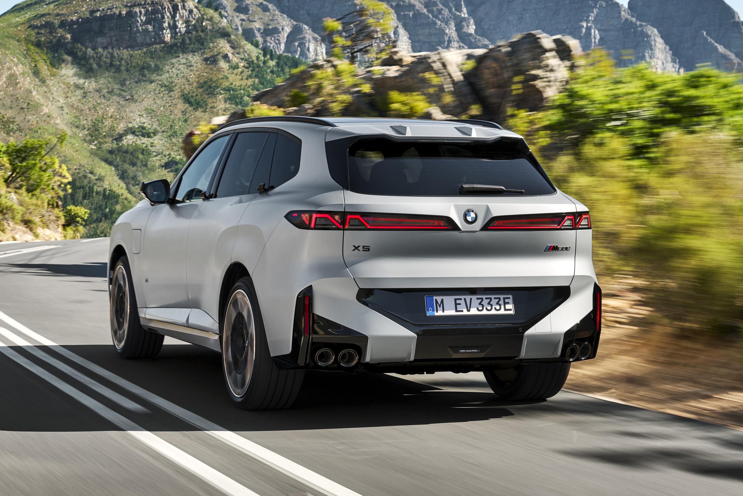 SUV BMW X5 cinza claro, visto por tr&aacute;s, em uma estrada sinuosa com montanhas e vegeta&ccedil;&atilde;o ao fundo