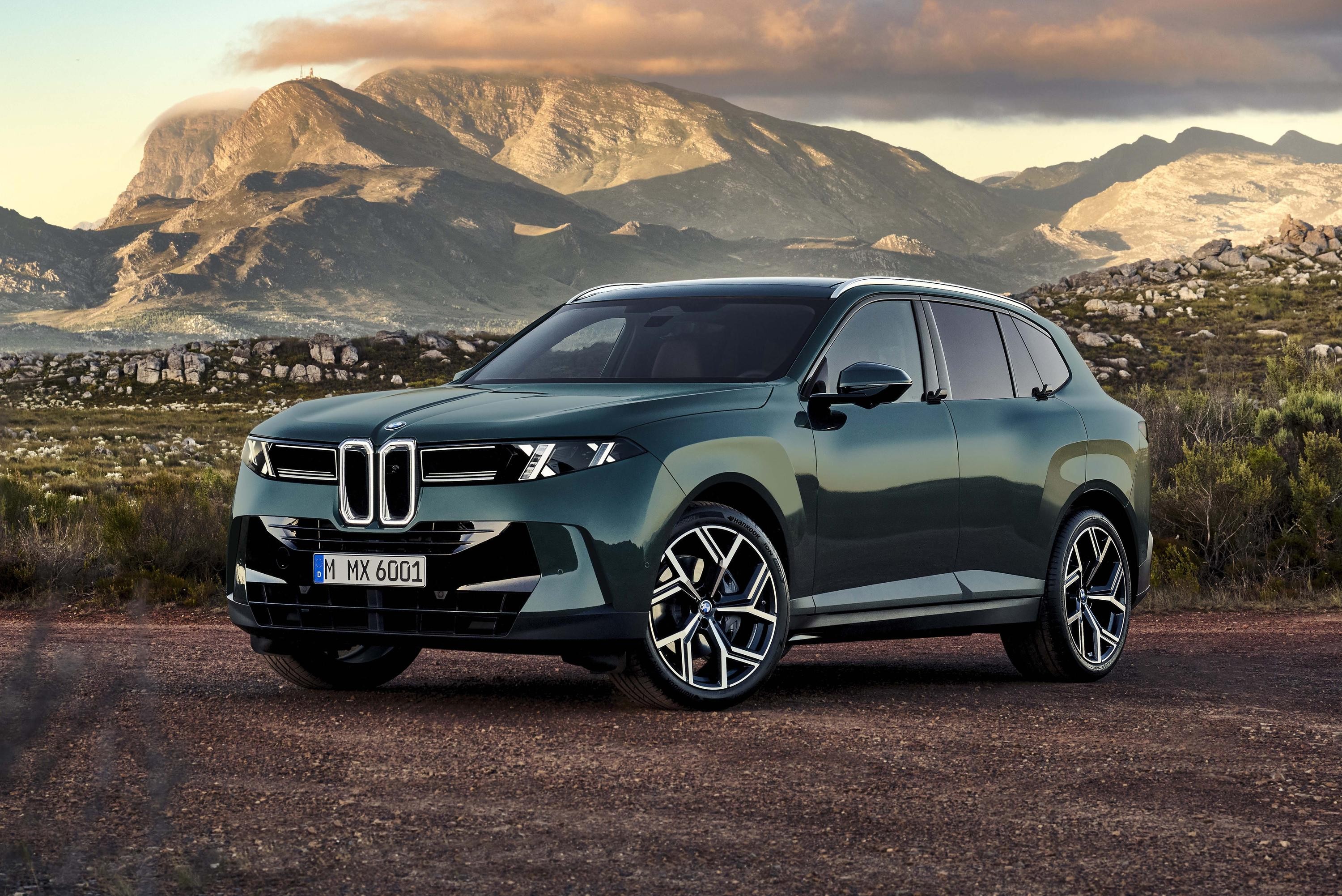 Um SUV verde-escuro com design moderno e far&oacute;is afilados, parado em uma estrada de terra. Ao fundo, montanhas rochosas sob um c&eacute;u com nuvens alaranjadas no p&ocirc;r do sol