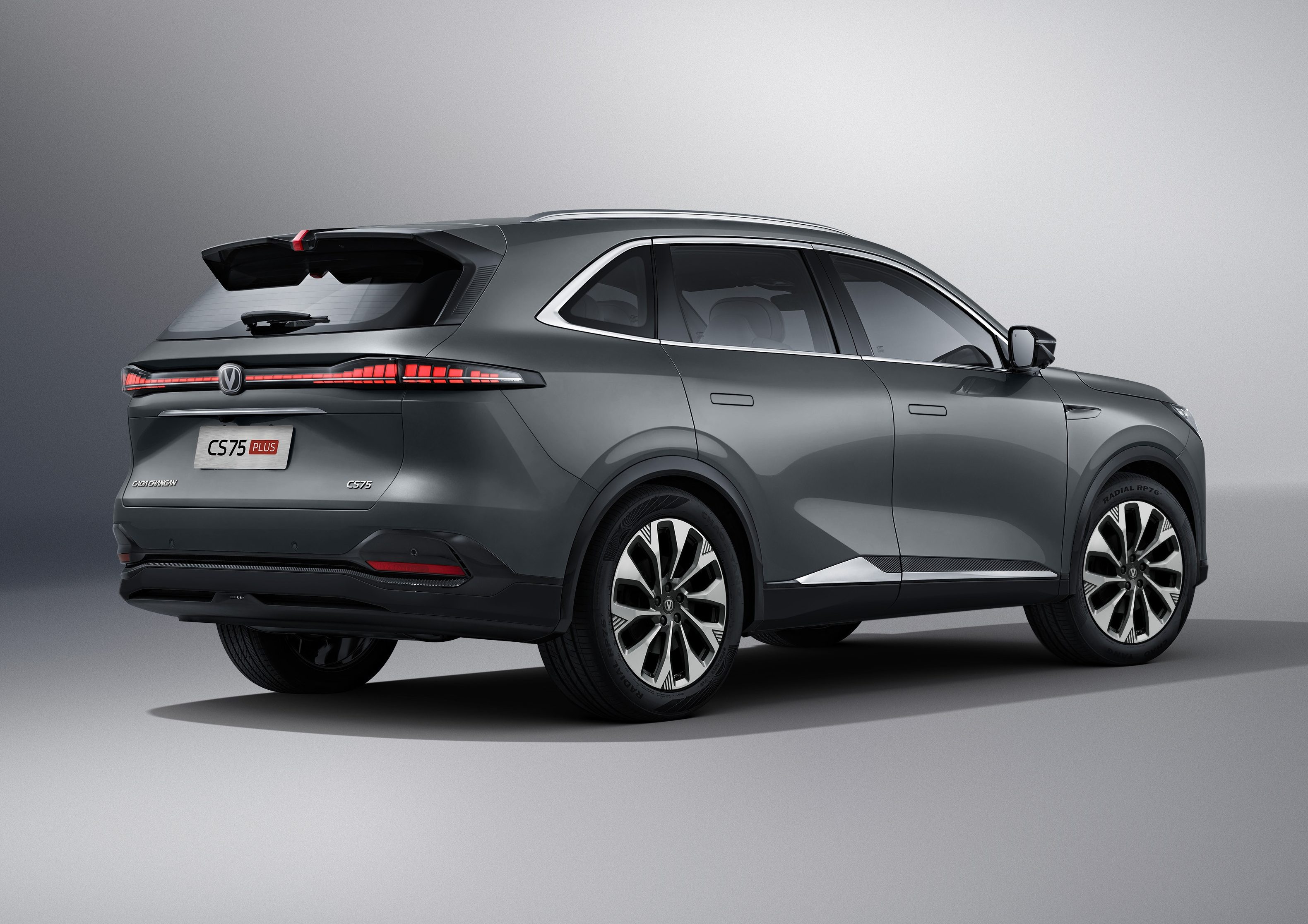 SUV cinza escuro, modelo Changan CS75 Plus, visto de traseira e lateral, parado em est&uacute;dio com fundo cinza claro. As lanternas traseiras est&atilde;o acesas, e as rodas t&ecirc;m design de estrela em preto e prata