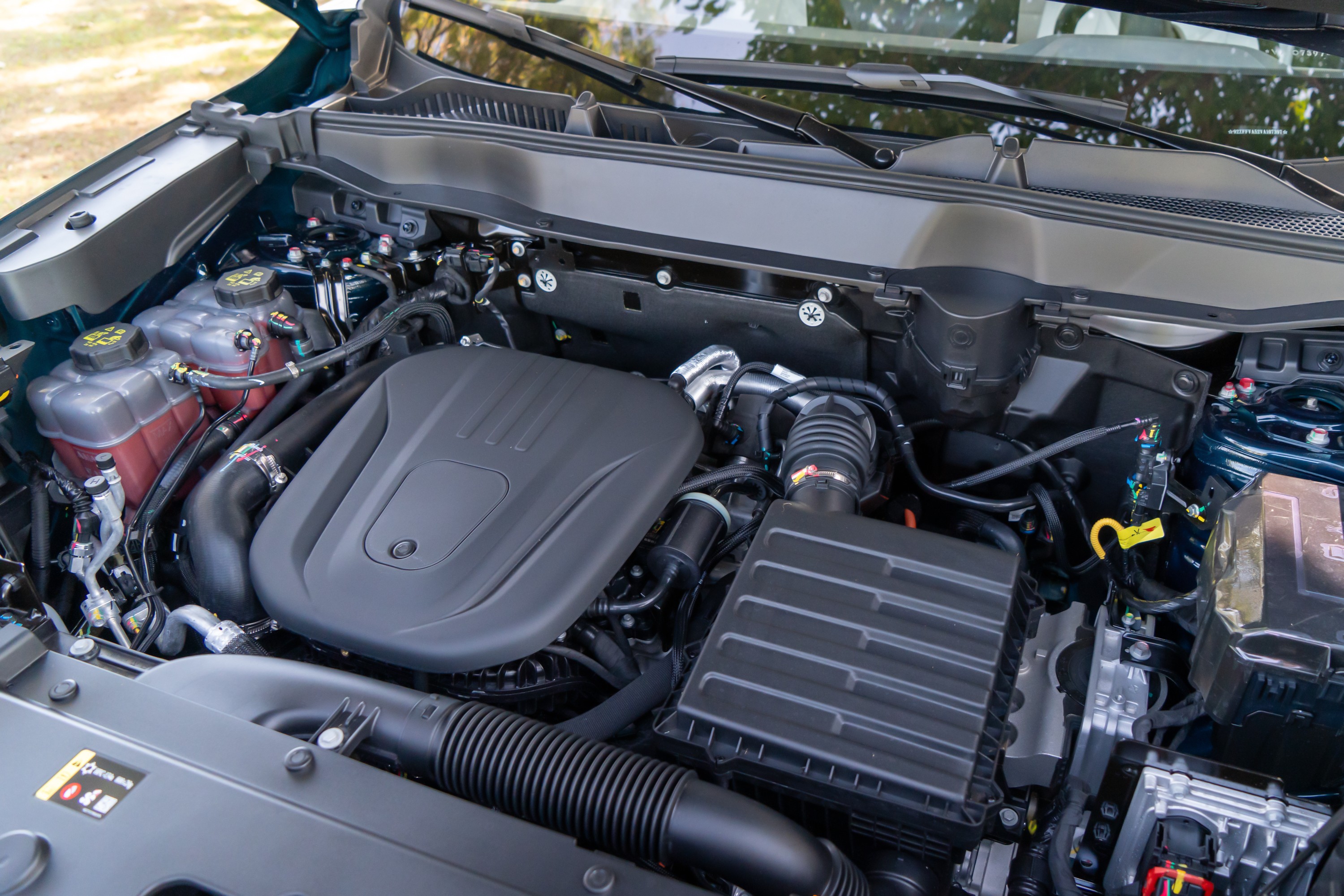 Compartimento do motor de um carro, com o motor coberto por uma capa preta, filtros de ar e reservat&oacute;rios de fluidos vis&iacute;veis