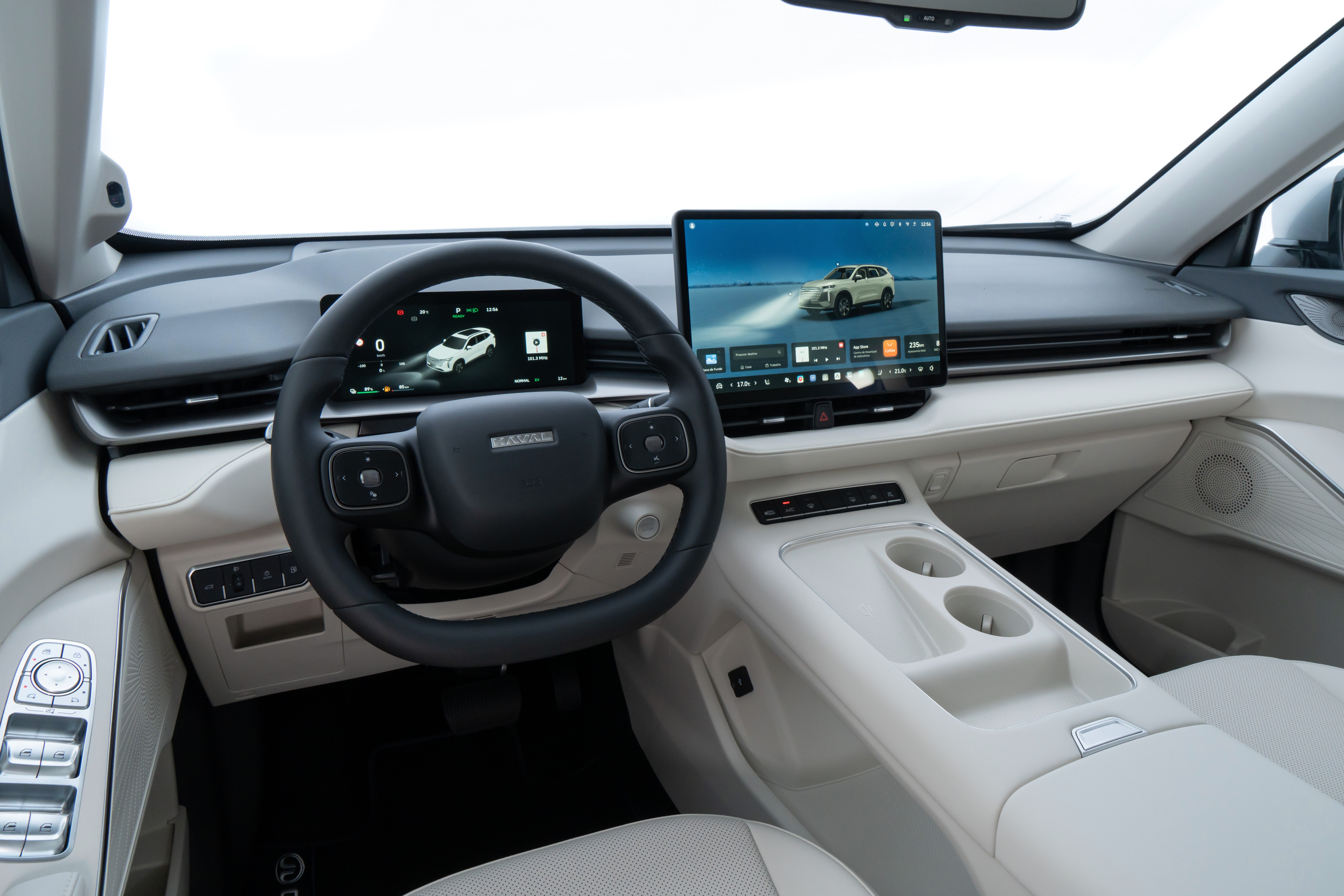 Interior moderno de um carro, com volante preto e painel claro. Dois monitores digitais exibem um SUV branco em diferentes cen&aacute;rios, um com far&oacute;is acesos. O console central tem porta-copos e bot&otilde;es de controle.