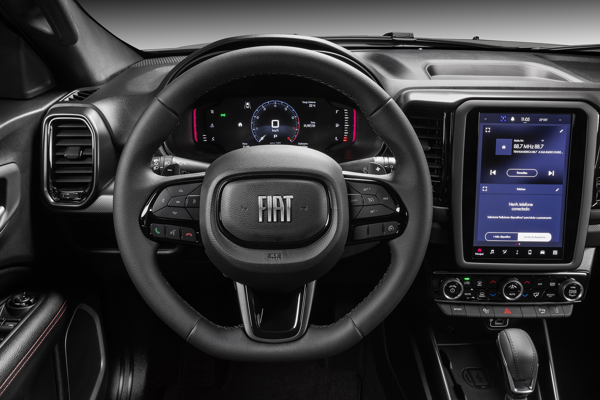 Interior de um carro moderno, com volante multifuncional preto e o logotipo Fiat no centro. &Agrave; esquerda, uma sa&iacute;da de ar retangular. Atr&aacute;s do volante, um painel digital com veloc&iacute;metro e informa&ccedil;&otilde;es do ve&iacute;culo. &Agrave; direita, uma tela multim&iacute;dia vertical exibindo r&aacute;dio e configura&ccedil;&otilde;es. Abaixo da tela, bot&otilde;es de controle e o c&acirc;mbio autom&aacute;tico