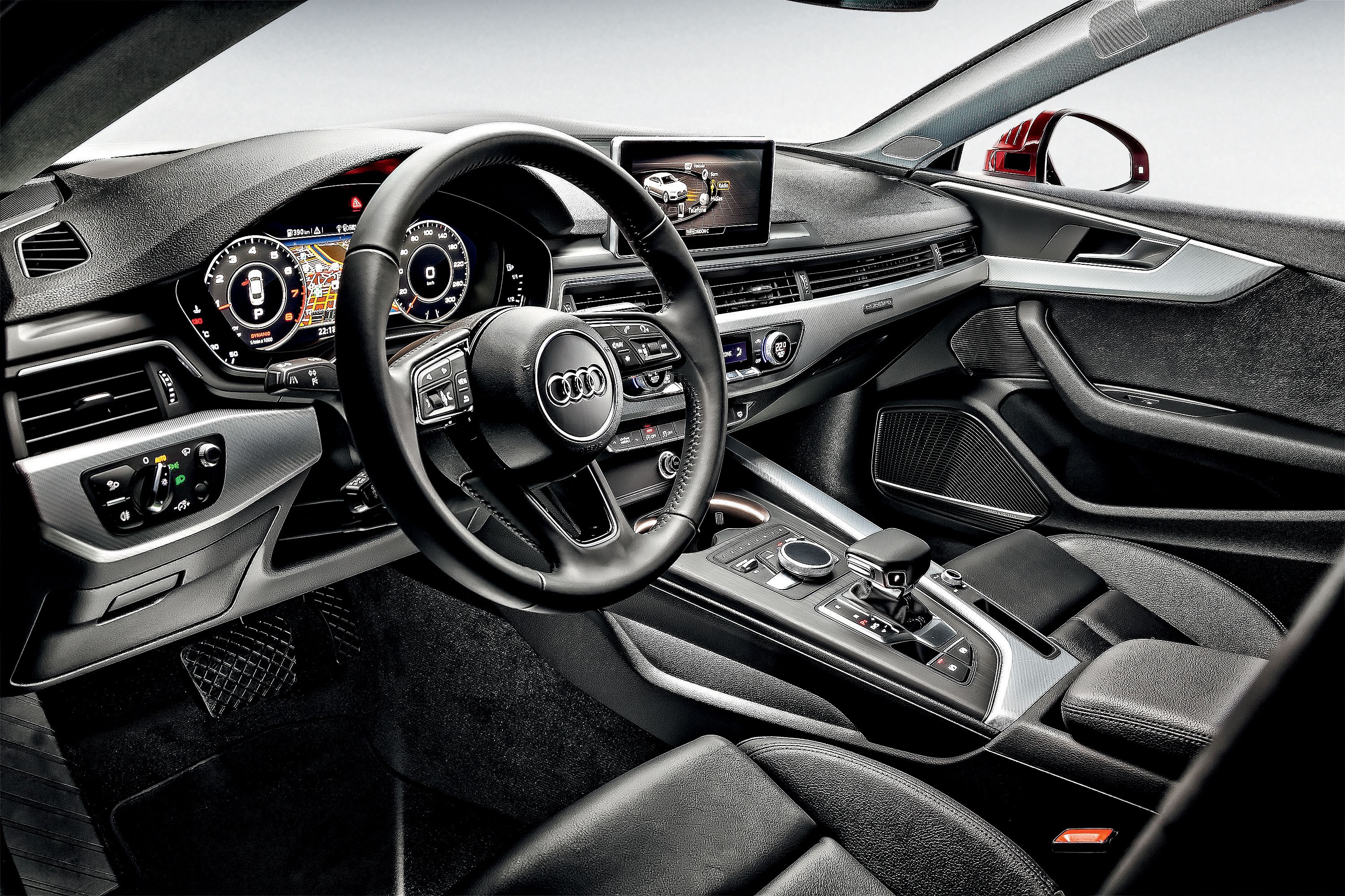 Interior de um carro Audi com acabamento em preto e detalhes prateados. O volante multifuncional de couro tem o logotipo da marca. O painel digital exibe informa&ccedil;&otilde;es do ve&iacute;culo e um mapa de navega&ccedil;&atilde;o. O console central possui c&acirc;mbio autom&aacute;tico, bot&otilde;es de controle e um apoio de bra&ccedil;o. O banco do motorista &eacute; de couro preto. A porta do passageiro tem detalhes prateados e um alto-falante. O espelho retrovisor lateral vermelho &eacute; vis&iacute;vel