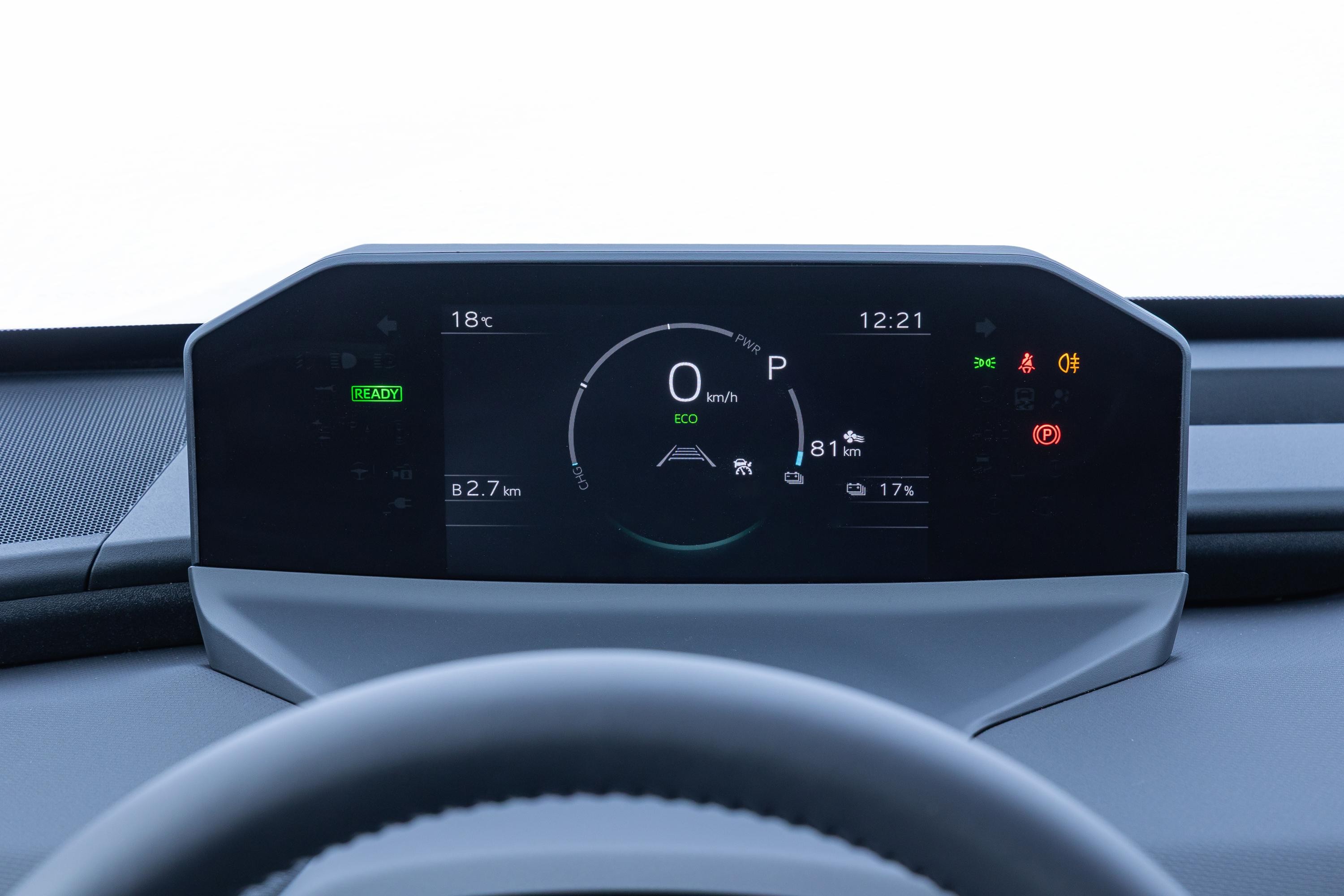 Painel digital de carro com informa&ccedil;&otilde;es como temperatura de 18&deg;C, hora 12:21, velocidade 0 km/h, modo ECO, dist&acirc;ncia de 81 km e bateria em 17%. Luzes indicadoras de farol, neblina e freio de m&atilde;o acesas. Volante escuro aparece na parte inferior