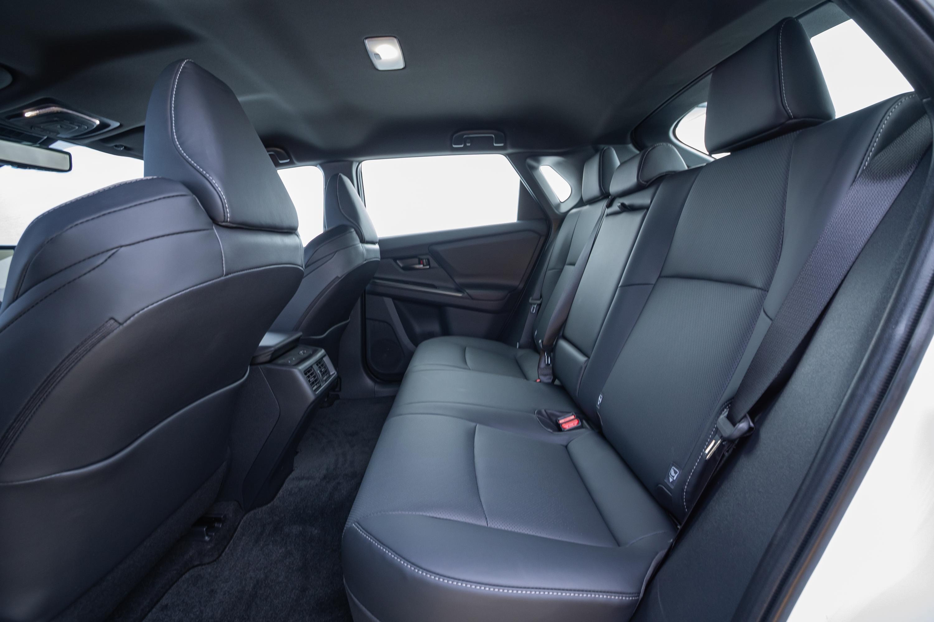 Interior de um carro com bancos traseiros de couro preto, costura branca e cintos de seguran&ccedil;a vermelhos. O teto &eacute; escuro, com uma luz acesa. As janelas laterais mostram um fundo branco. O piso &eacute; forrado com carpete escuro.