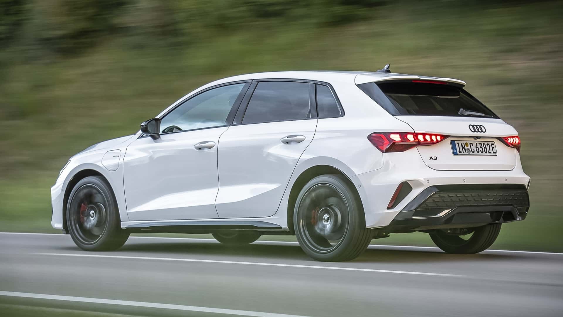 Audi A3 Sportback branco, visto de lado e traseira, em movimento r&aacute;pido numa estrada asfaltada com faixa branca, com fundo verde borrado