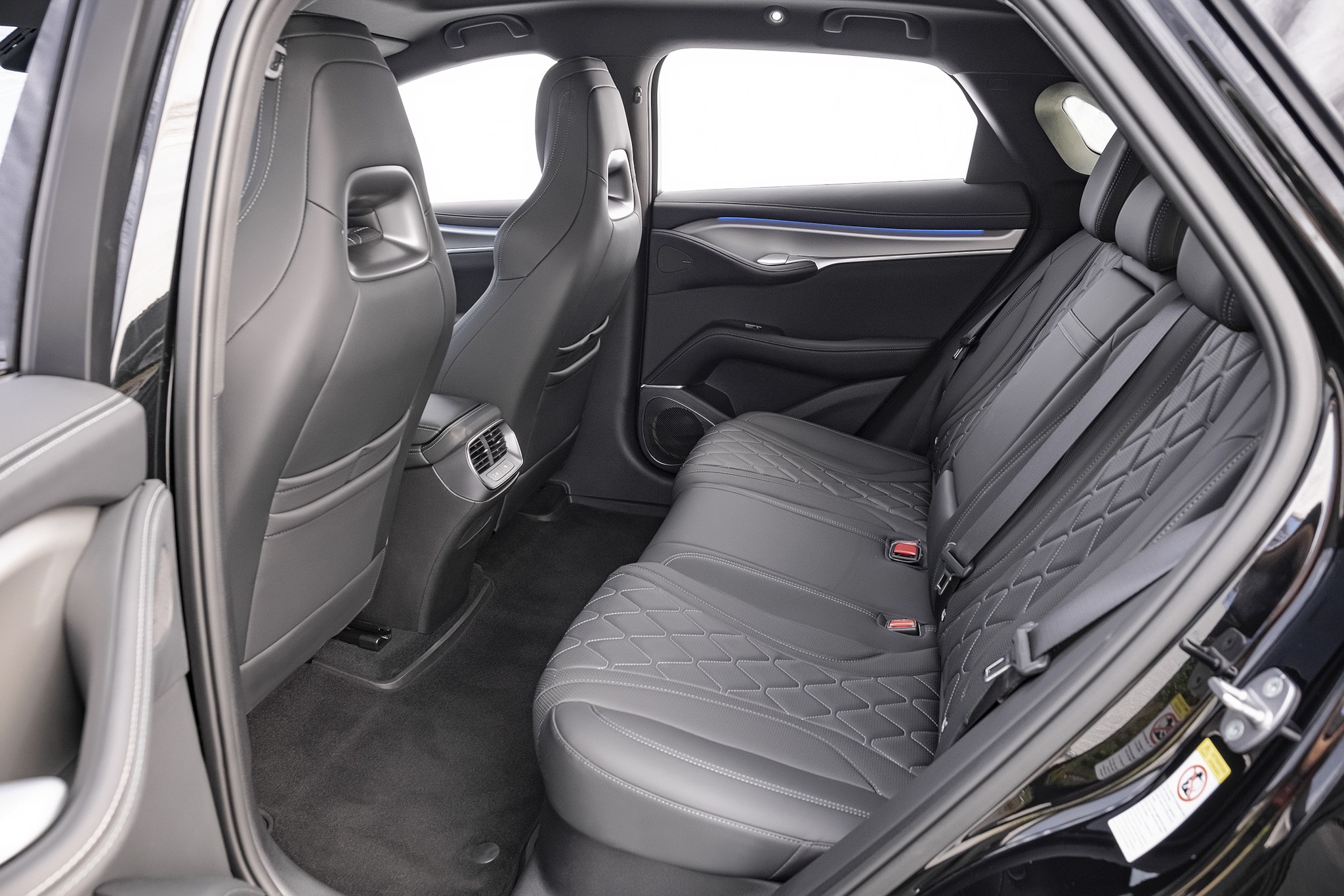 Interior de um carro com bancos traseiros de couro preto e costura em losango, vistos da porta traseira aberta. Os bancos dianteiros tamb&eacute;m s&atilde;o pretos, com detalhes prateados nos encostos. O piso &eacute; escuro e as janelas mostram um fundo branco