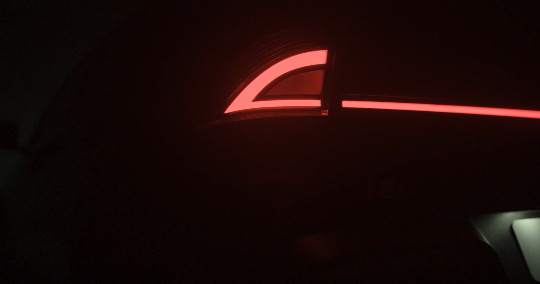 Lanterna traseira de carro com luzes LED vermelhas em formato de L e uma linha horizontal, em ambiente escuro