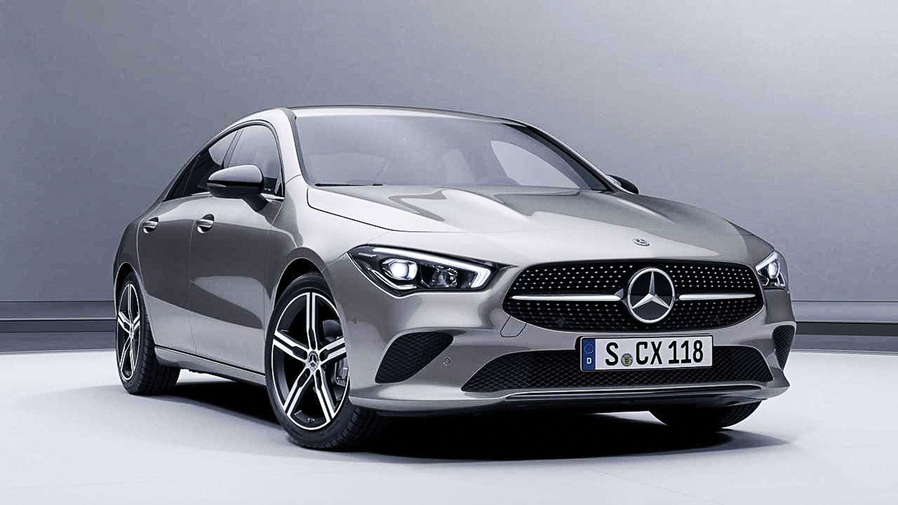 Carro Mercedes-Benz CLA prateado, visto de frente e ligeiramente &agrave; direita, com far&oacute;is acesos, grade frontal pontilhada e placa S CX 118, em fundo cinza claro