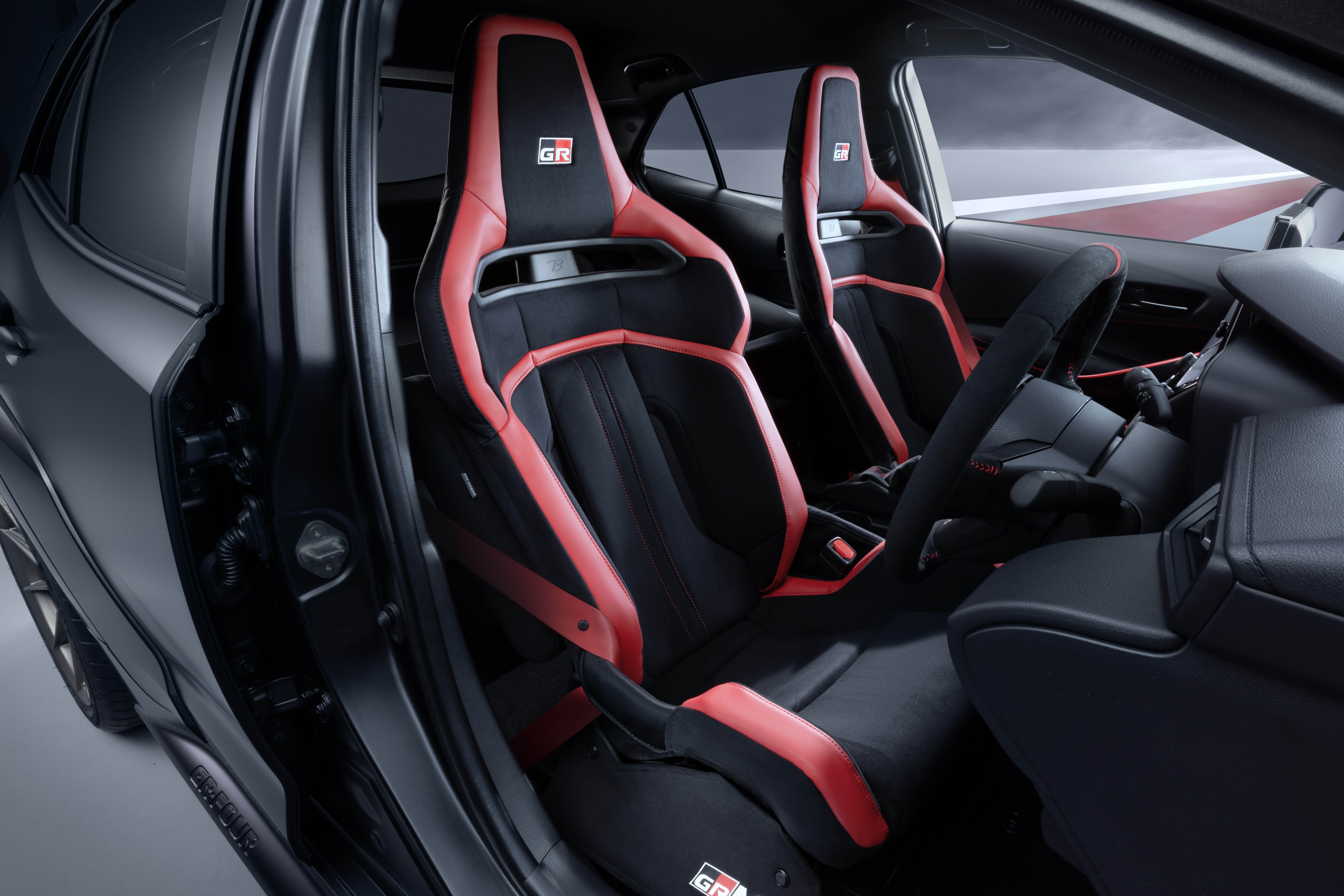 Interior de carro esportivo com dois bancos dianteiros pretos e detalhes vermelhos, incluindo o logotipo 