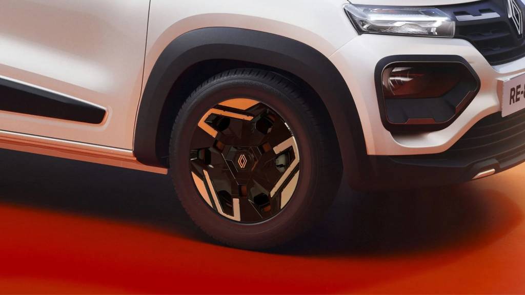 Parte frontal de um carro branco com detalhes em preto, incluindo a roda dianteira com calota preta e detalhes em laranja, para-lama preto e farol aceso. O ve&iacute;culo est&aacute; sobre um fundo laranja