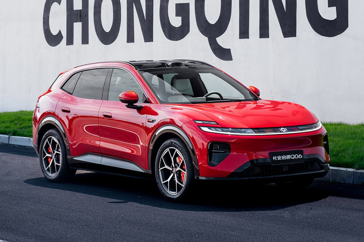 SUV vermelho brilhante, modelo Changan Q06, estacionado em asfalto escuro com uma parede branca e grama verde ao fundo. O carro tem teto preto, rodas esportivas e far&oacute;is de LED finos. O nome CHONGQING est&aacute; escrito em letras grandes e pretas na parede