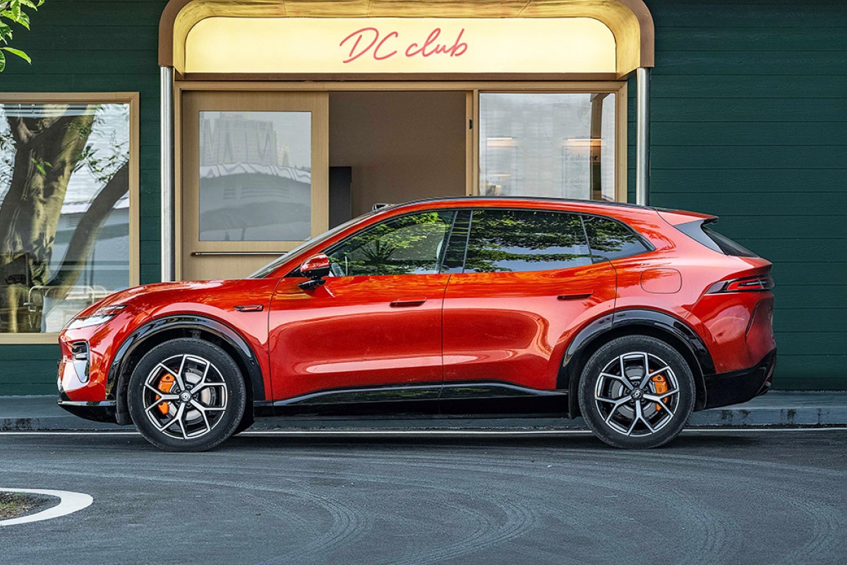 SUV vermelho brilhante estacionado de perfil em frente a um pr&eacute;dio verde escuro com uma placa iluminada DC club acima da porta