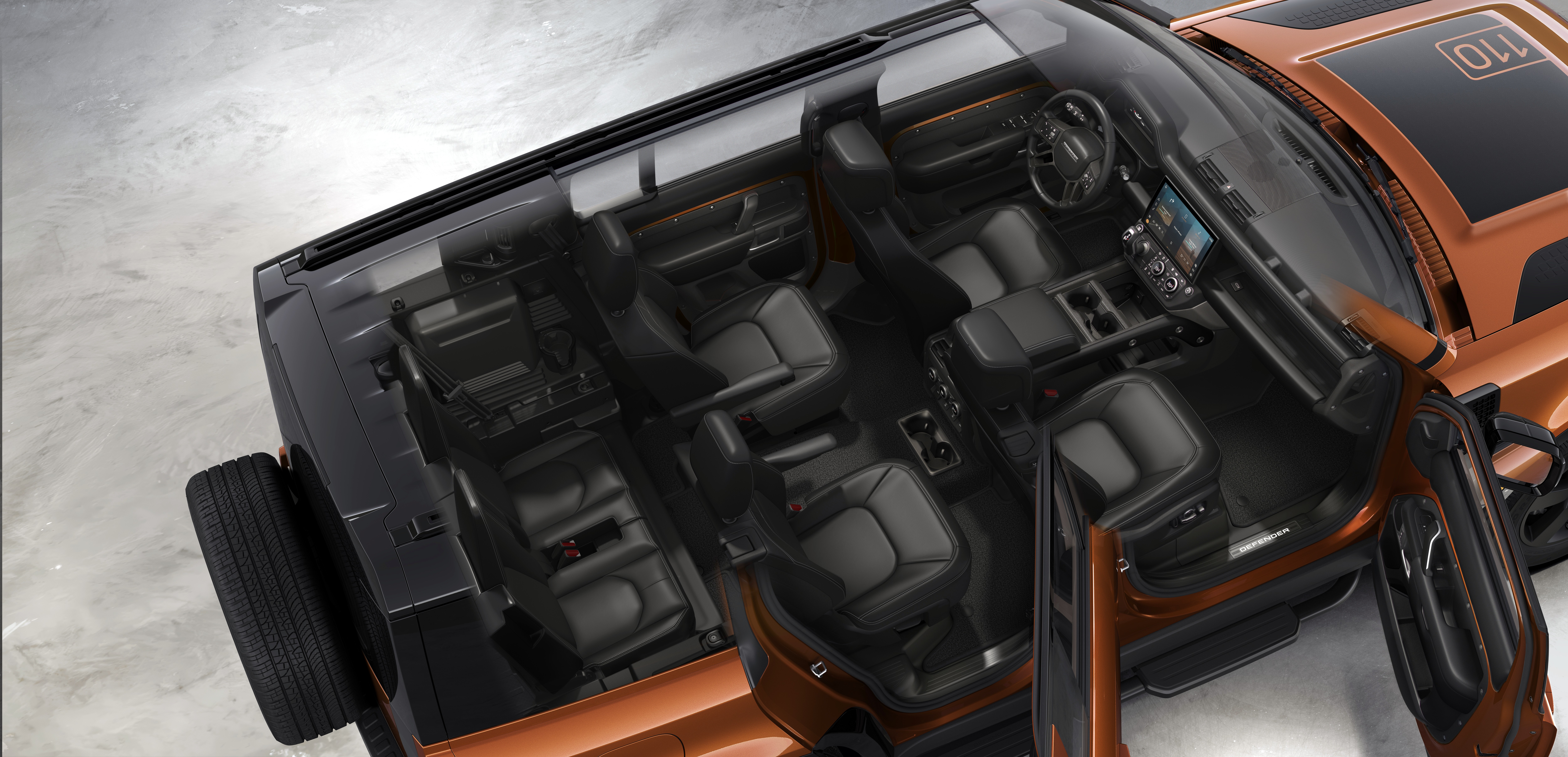 Vista a&eacute;rea do interior de um carro SUV laranja com teto preto, mostrando os bancos de couro escuro e o painel com tela digital. A porta do passageiro est&aacute; aberta, revelando o espa&ccedil;o interno e o pneu sobressalente na traseira.