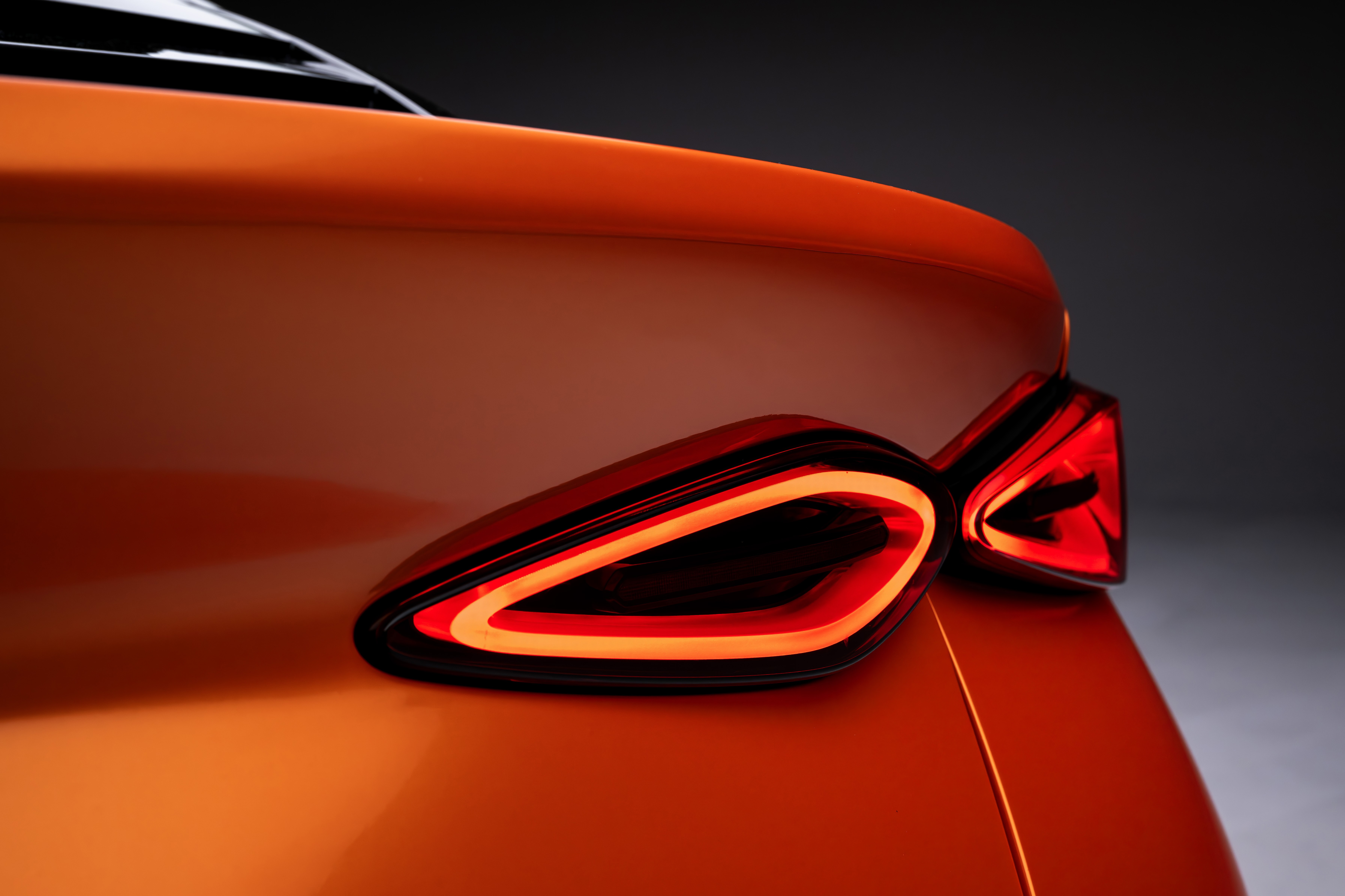 Traseira de um carro esportivo laranja, com lanternas de LED acesas em formato de bumerangue, emitindo luz vermelha e laranja, contra um fundo escuro
