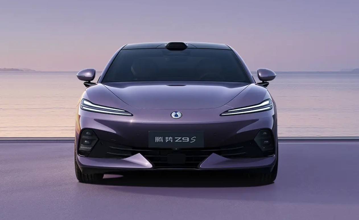 Carro el&eacute;trico Denza Z9 GT roxo com far&oacute;is em LED acesos, parado em uma estrada &agrave; beira-mar ao entardecer