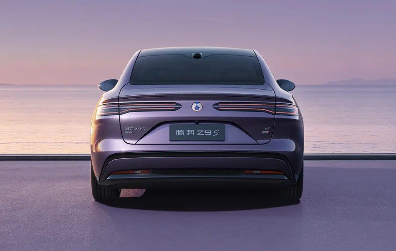 Traseira de um carro roxo escuro, com lanternas horizontais finas e o nome 腾势 Z9 S na placa, estacionado em uma superf&iacute;cie roxa clara. Ao fundo, um oceano calmo sob um c&eacute;u em tons de roxo e rosa no p&ocirc;r do sol