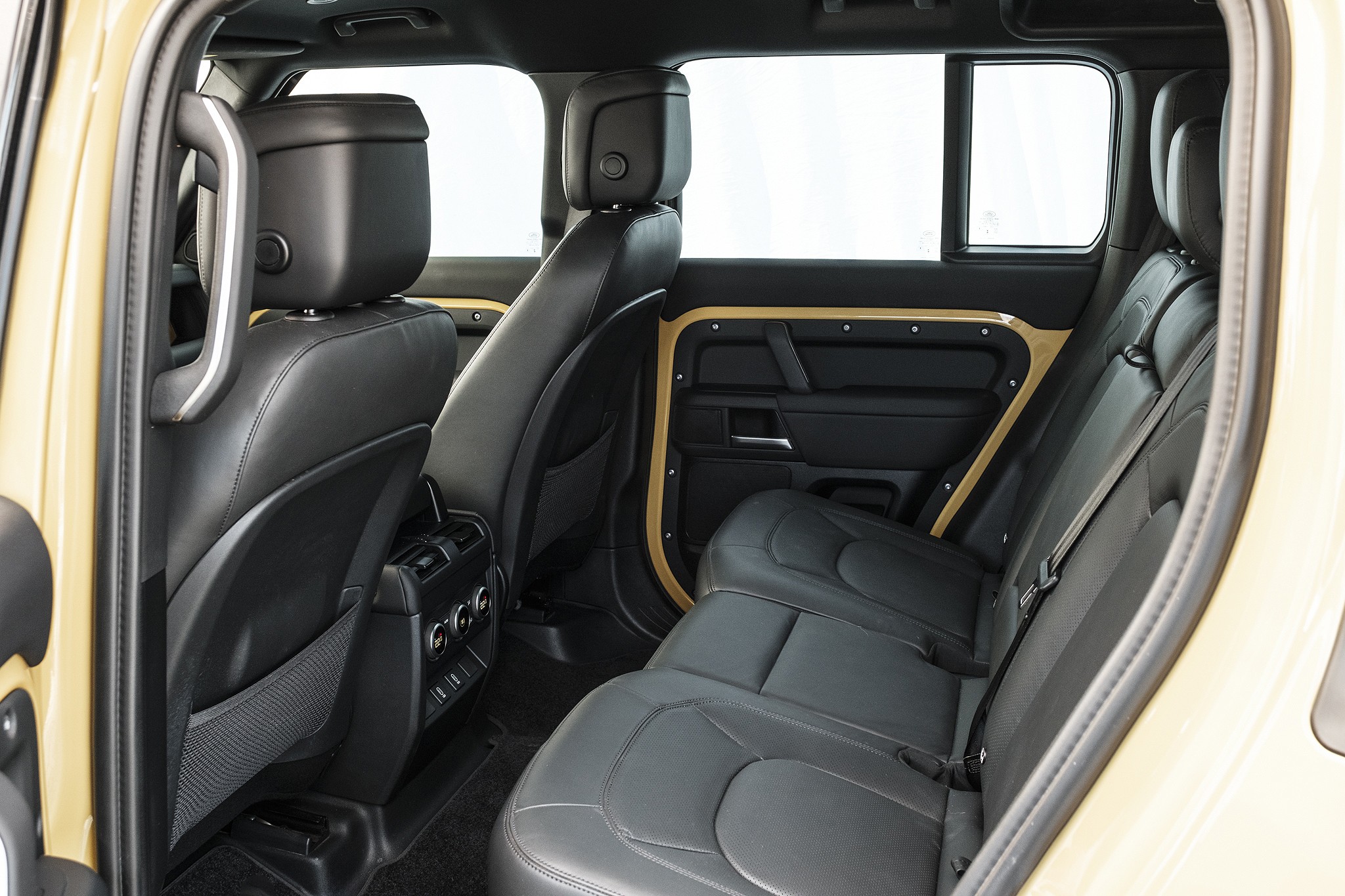 Interior de um carro bege, mostrando os assentos traseiros de couro preto com cintos de seguran&ccedil;a e detalhes dourados nas portas