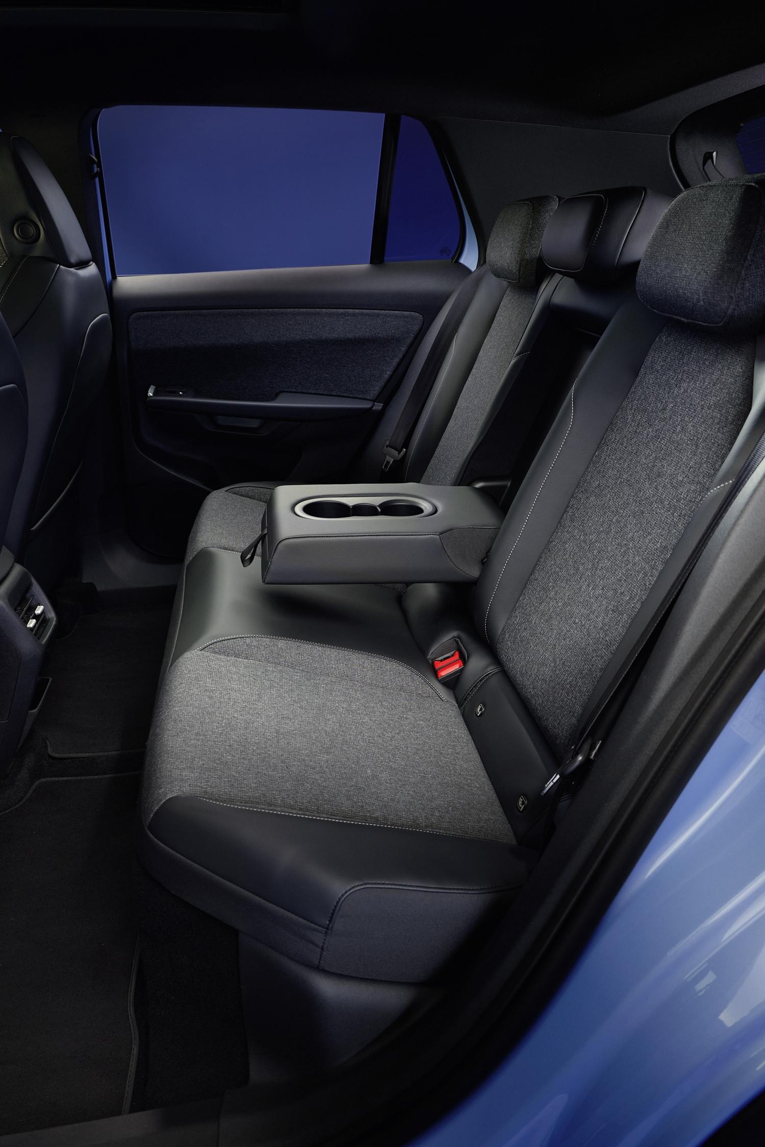 Interior de um carro com bancos traseiros em tecido cinza e detalhes em couro preto, com um apoio de bra&ccedil;o central rebat&iacute;vel com porta-copos. O assoalho &eacute; preto e a janela exibe um tom azul escuro