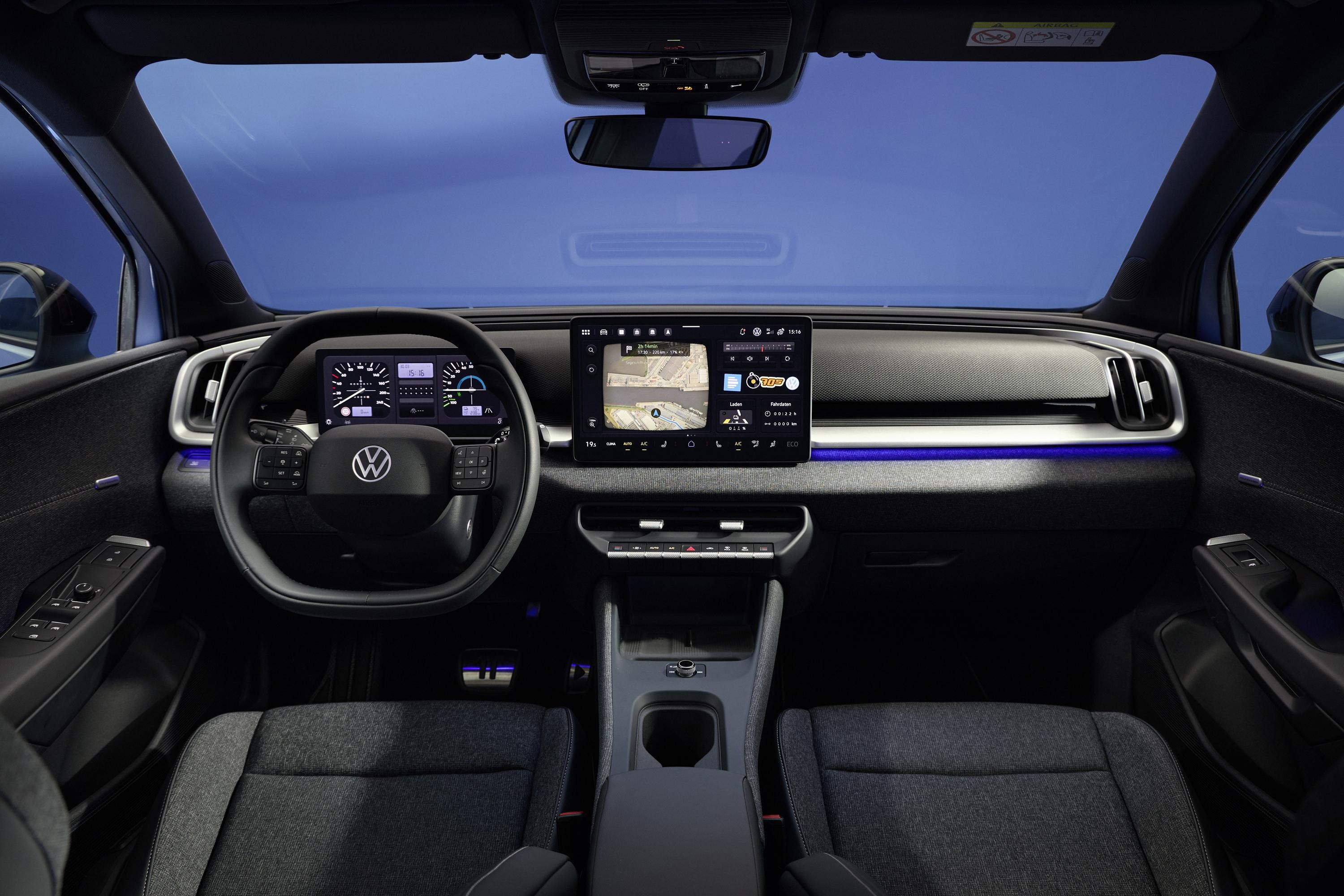 Interior de um carro moderno com volante preto, painel digital e tela multim&iacute;dia central exibindo um mapa. H&aacute; uma faixa de luz azul no painel e bancos de tecido escuro. O para-brisa mostra um c&eacute;u azul